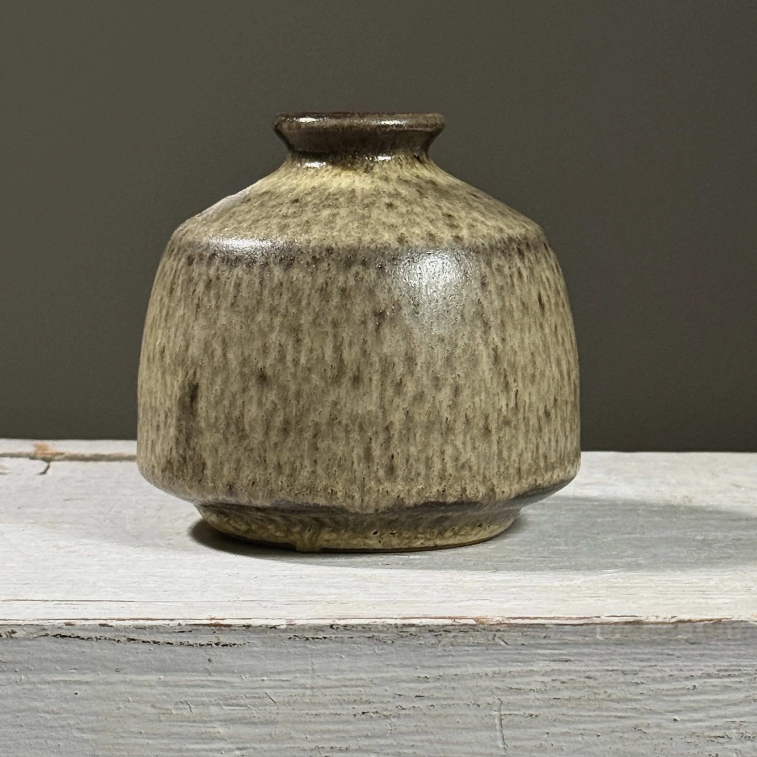 Front view of a vintage Japanese glazed ceramic vessel with pale green and brown drip glaze.