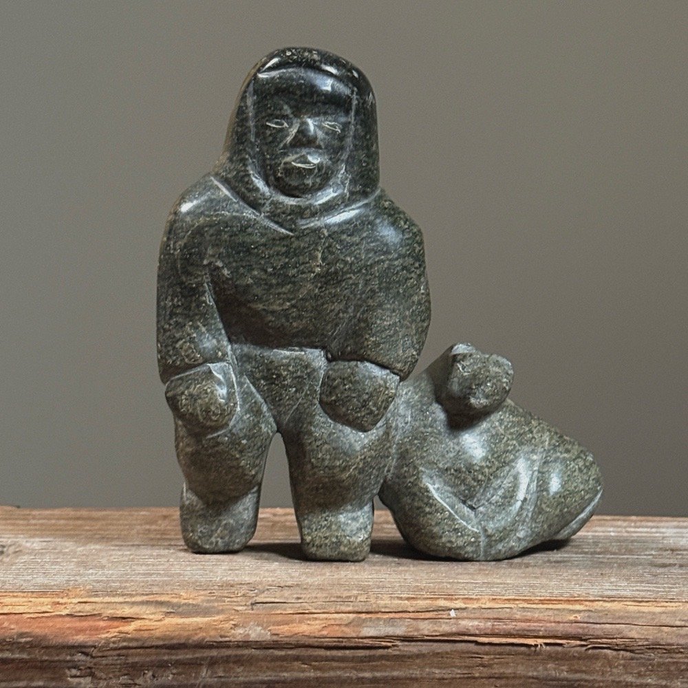 Full frontal view of a vintage Inuit hand-carved green soapstone sculpture of a human figure with a seal