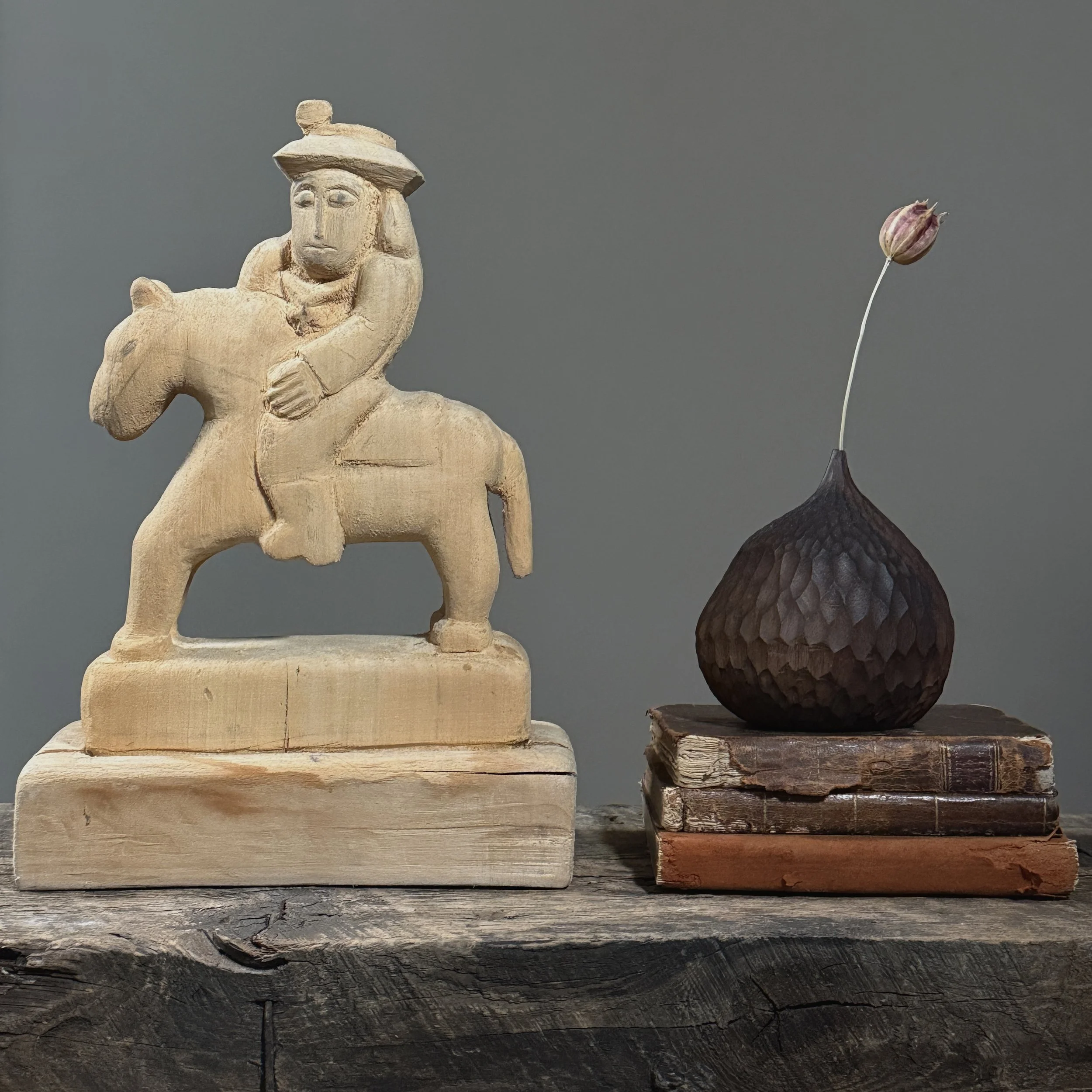 Front view of a vintage hand-carved wooden horse and rider sculpture With books for size reference.