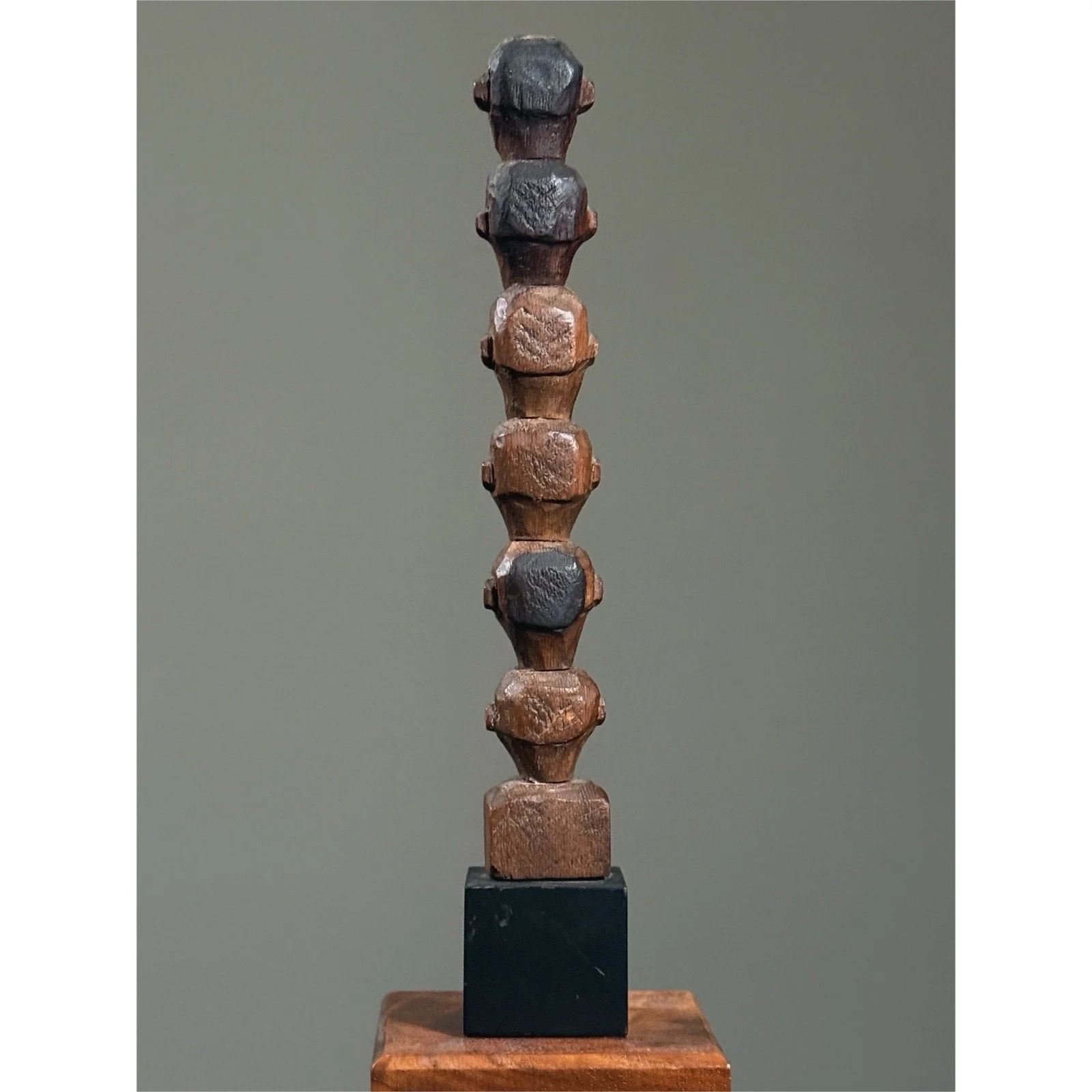 Antique totem sculpture with multiple carved heads, back view.