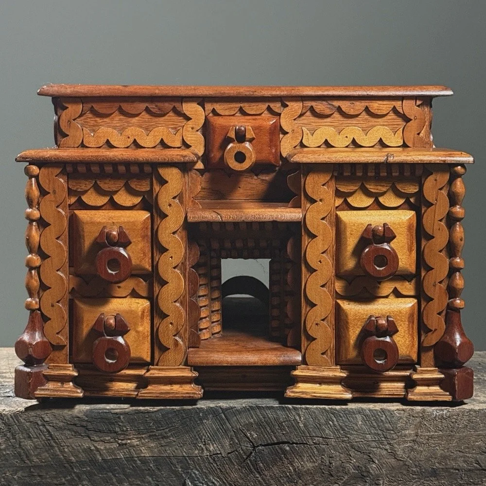 Full frontal view of a vintage folk art box with seven drawers and heavy layered scrollwork