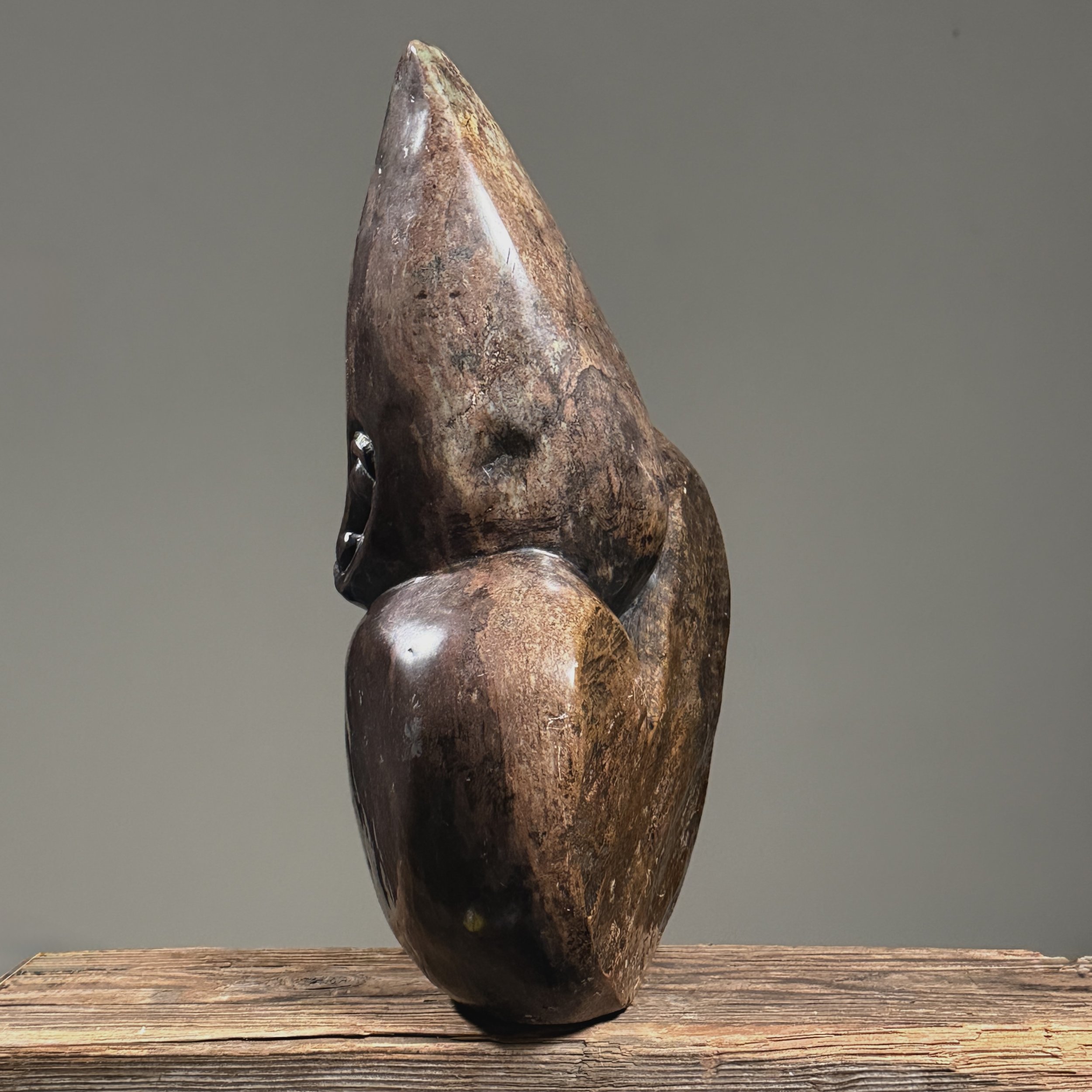 Side view of vintage figurative Shona stone sculpture, 13.5 inches tall, elongated head, puce-colored material.