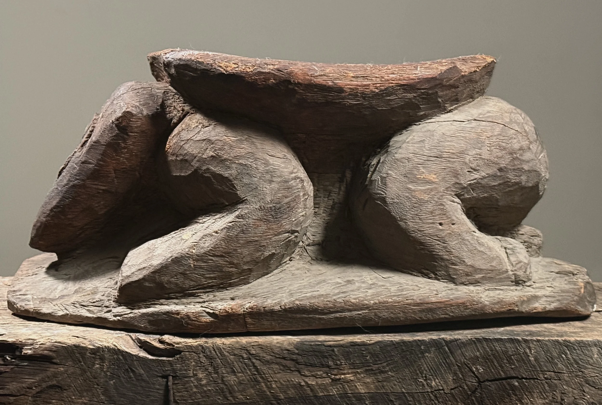 Side profile of a Melanesian anthropomorphic stool showing the figure's posture and stool proportions