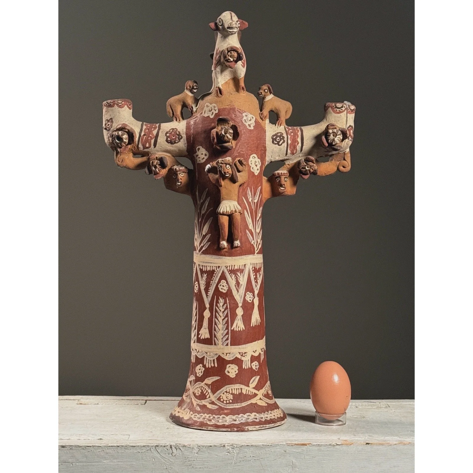 Full frontal view of a vintage polychrome folk art candelabra with Jesus and animal figures with egg for size reference.