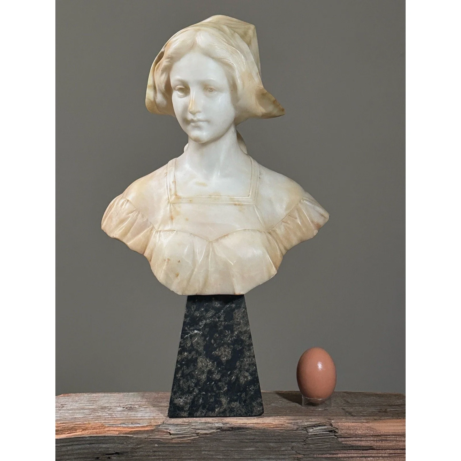 Full frontal view of the Art Nouveau alabaster bust of a woman on its marble base with egg for size reference.