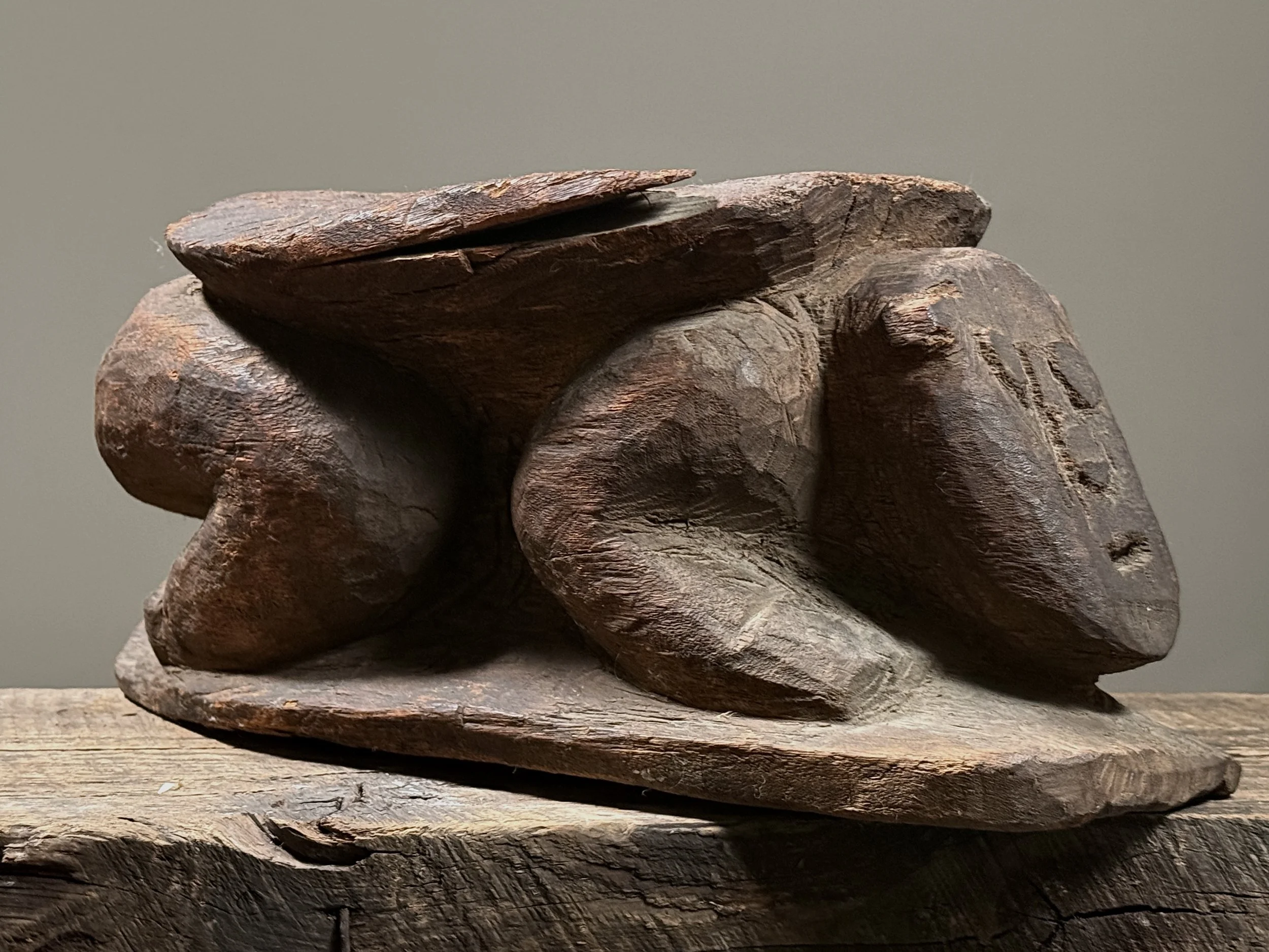 Three-quarter view of a hand-carved wooden stool with figural support and carved top surface
