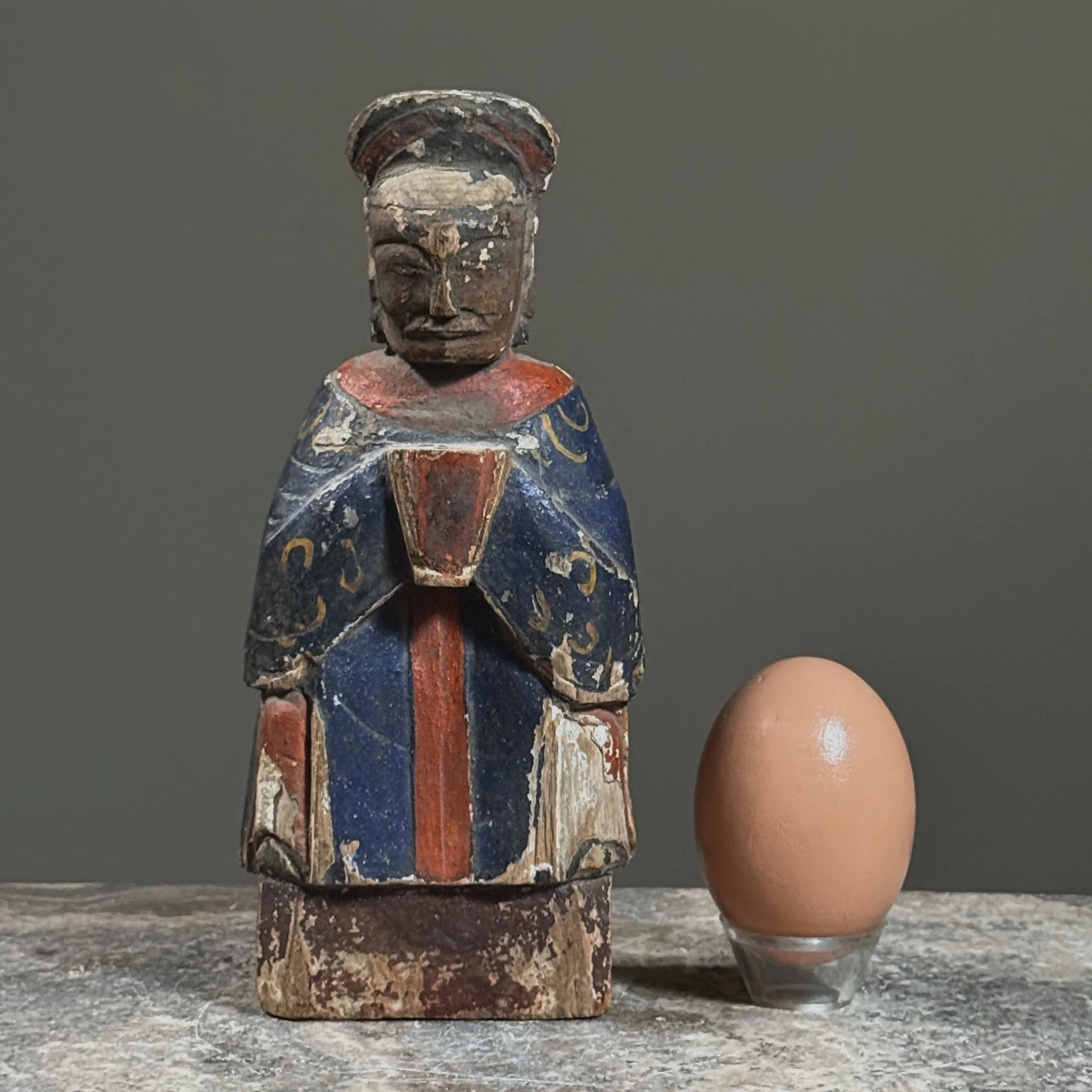 Front view of a Qing Dynasty polychrome gilt wooden deity figure with egg for size reference.