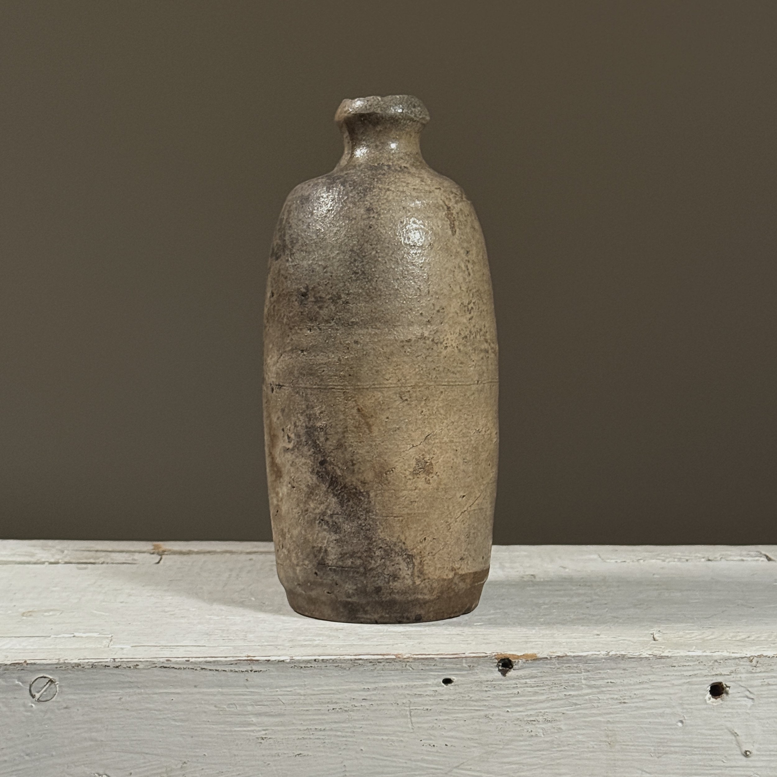 Front view of a Japanese ash-glazed stoneware tokkuri (sake bottle).