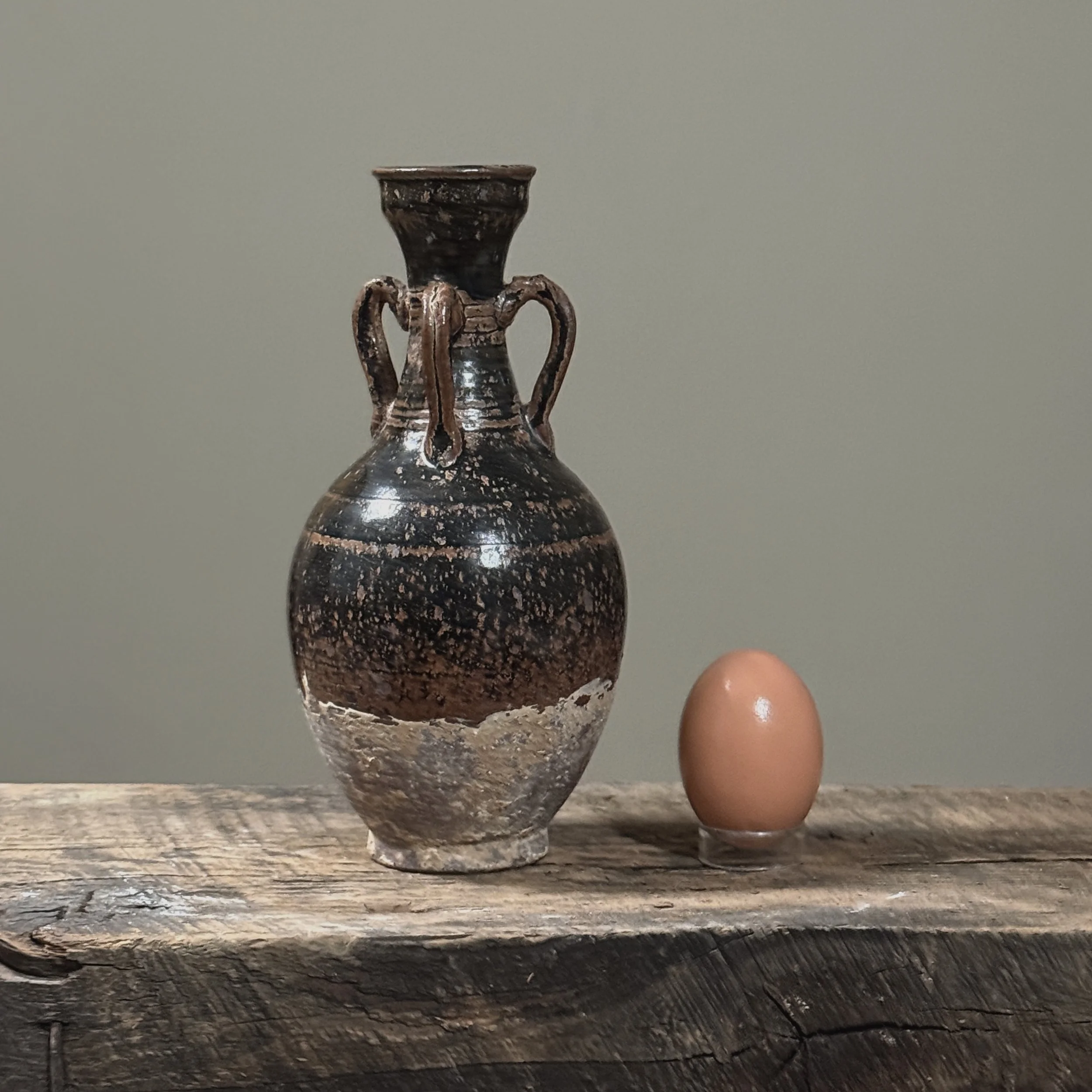 Full front view of antique four handled brown speckled glazed stoneware vessel, Cizhou kiln style amphora, 8 inches tall With egg for size reference