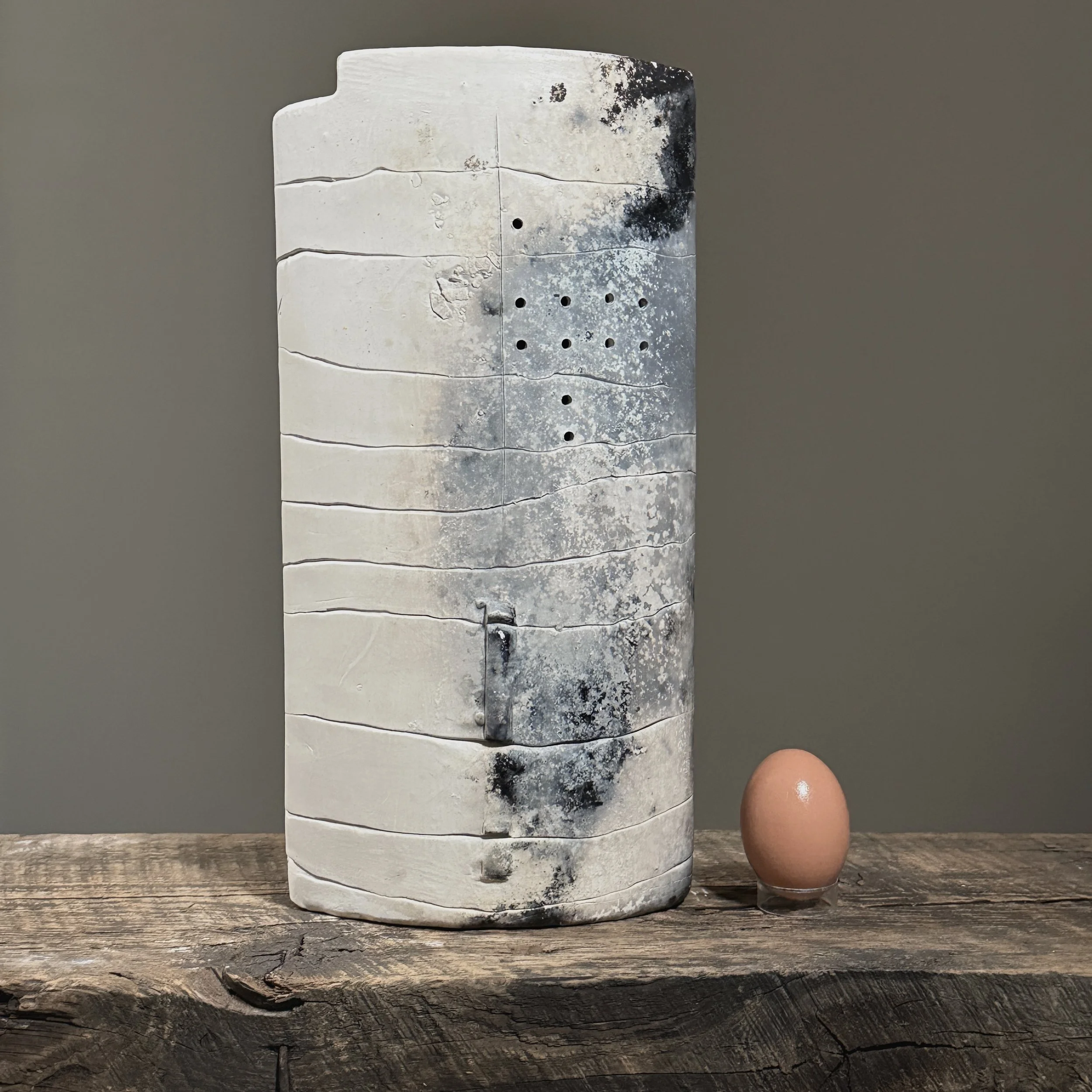 White raku ceramic form with ash deposits with egg for size reference.