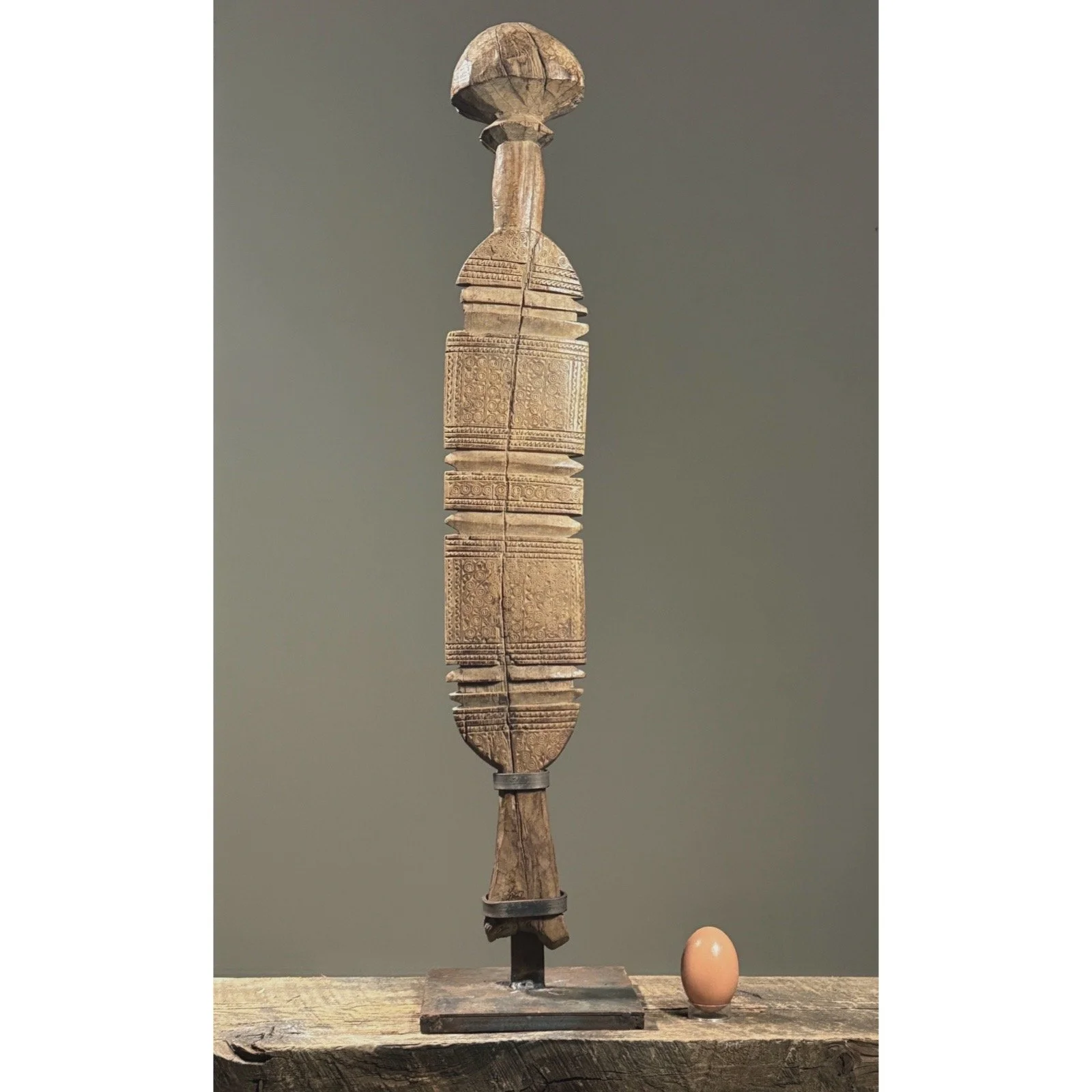 Full view of an antique Tuareg carved tent pole mounted on an iron stand with egg for size reference.