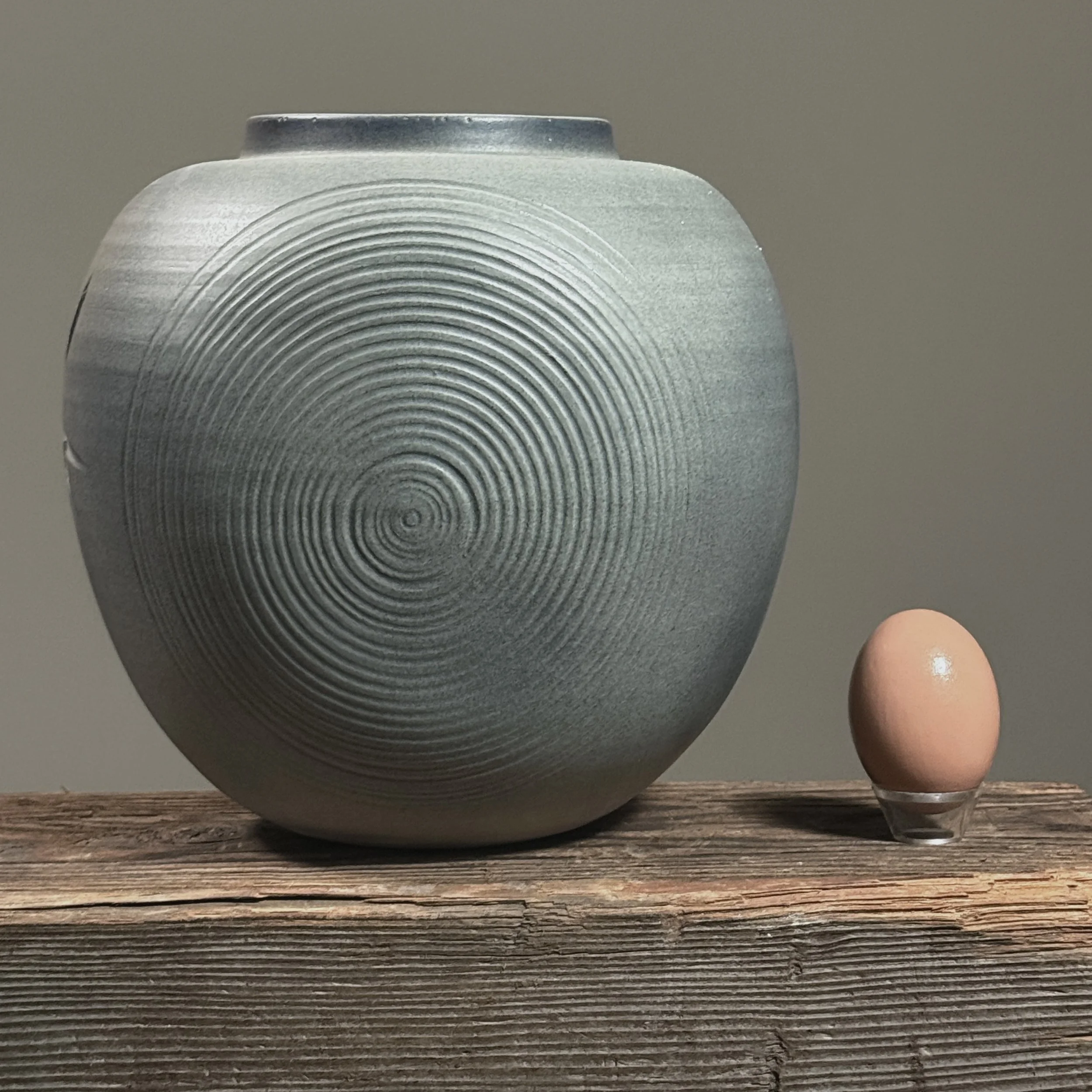 Side view showing swirl motif on Japanese minimalist vase with egg for size reference.
