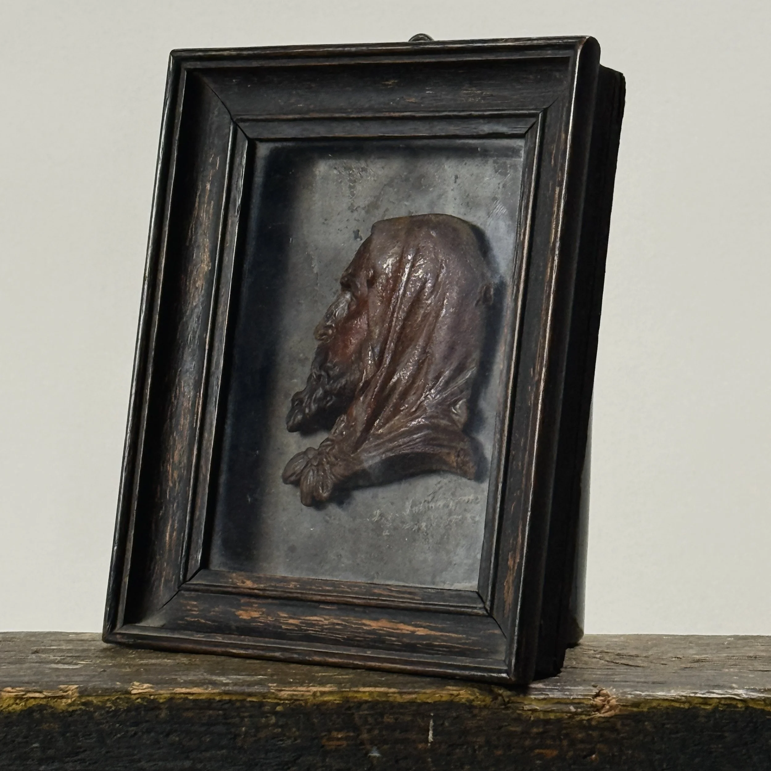 Three-quarter view of antique French wax bas-relief showing frame and glass covering the red wax profile