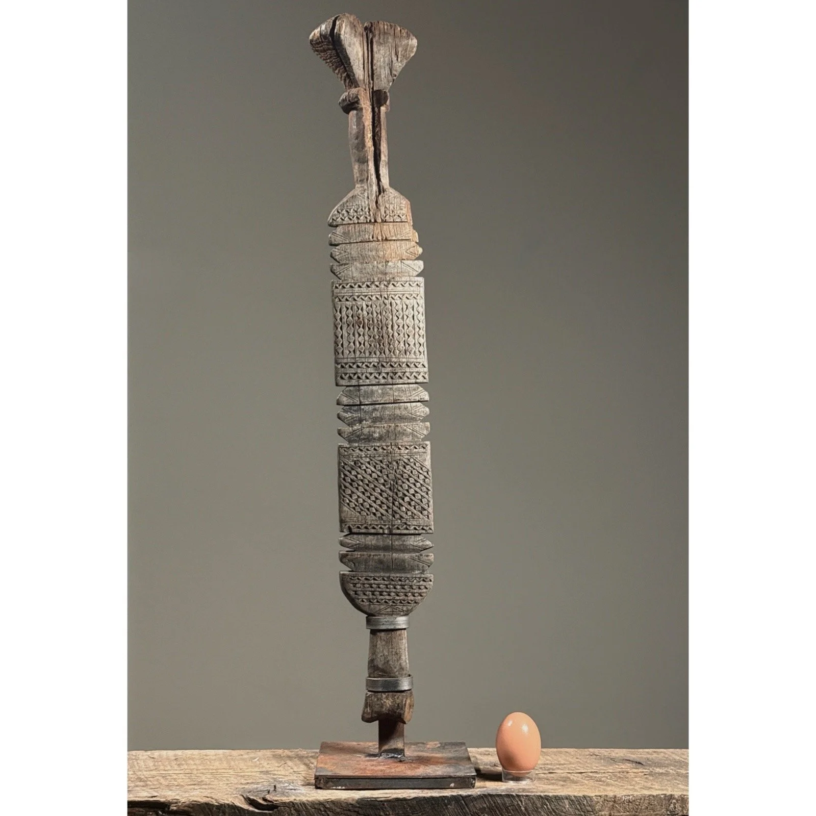 Full view of an antique Tuareg hand-carved wooden tent pole on custom iron stand with egg for size reference.