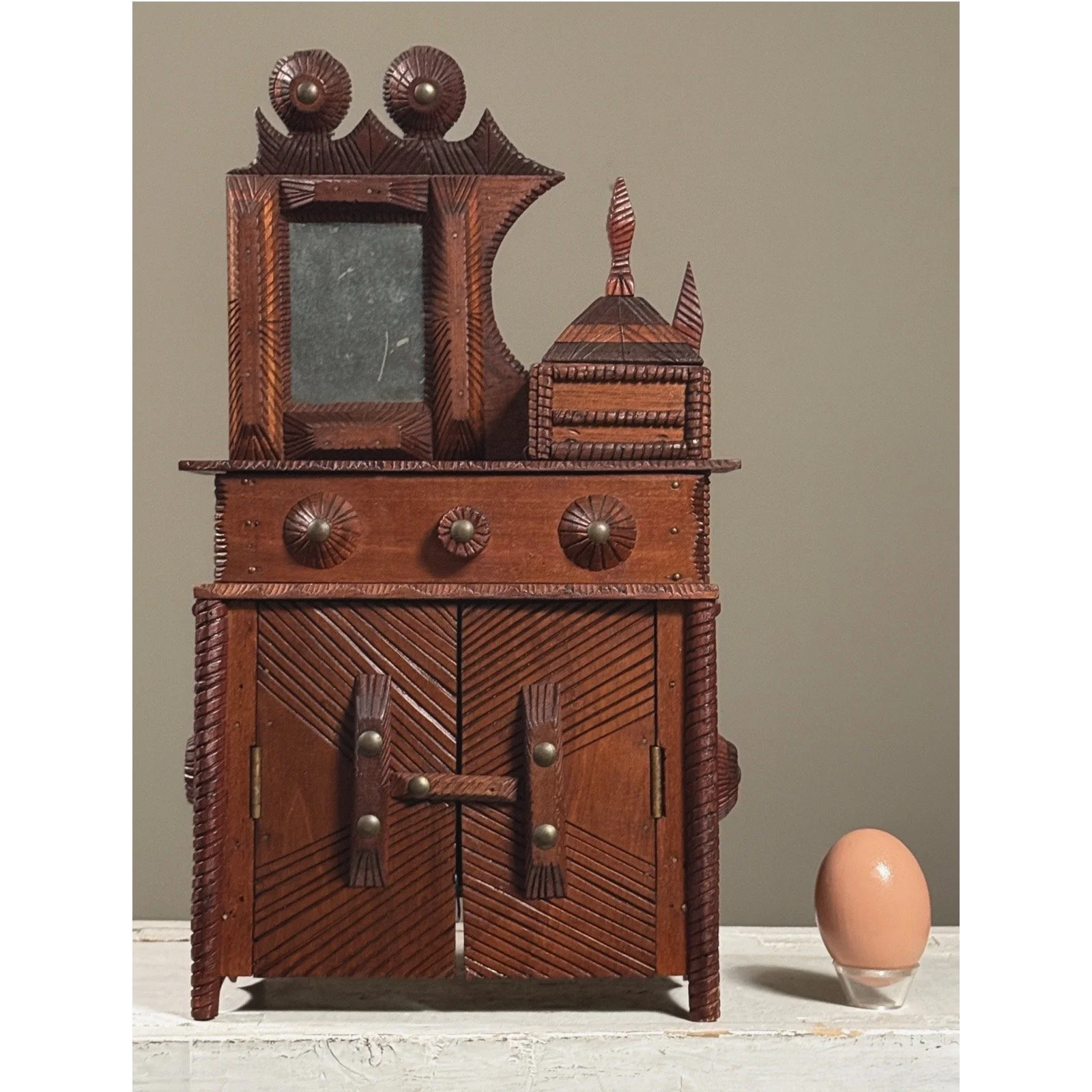 Full view of antique chip-carved tramp art miniature dresser With egg for size comparison.