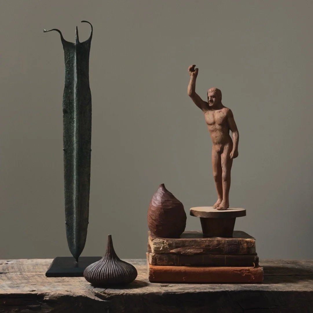 Vintage folk art hand carved male nude sculpture on tapered stand in a vignette.