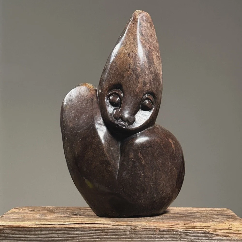 Front view of vintage figurative Shona stone sculpture, 13.5 inches tall, elongated head, puce-colored material.