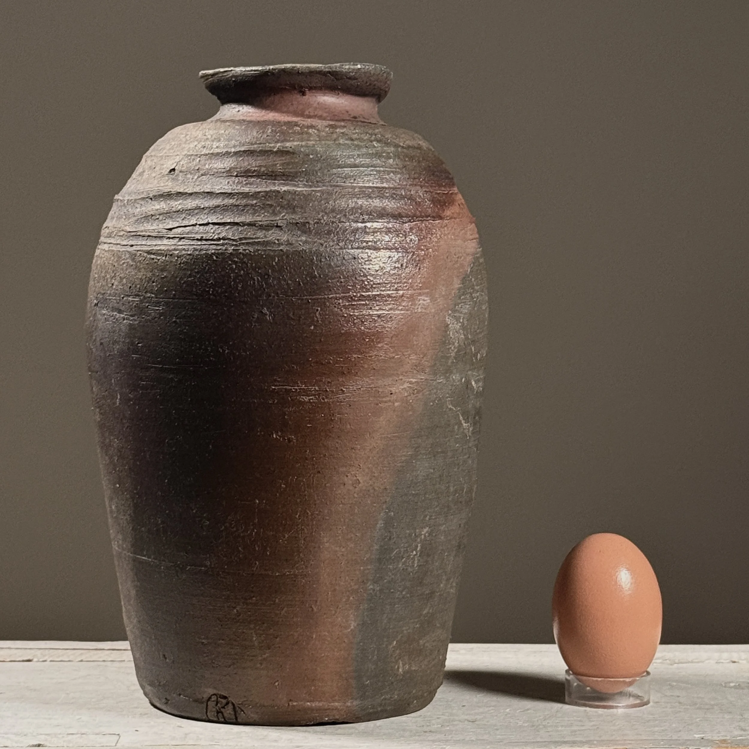Front view of a vintage wabi-sabi wood-fired stoneware vessel with egg for size reference.
