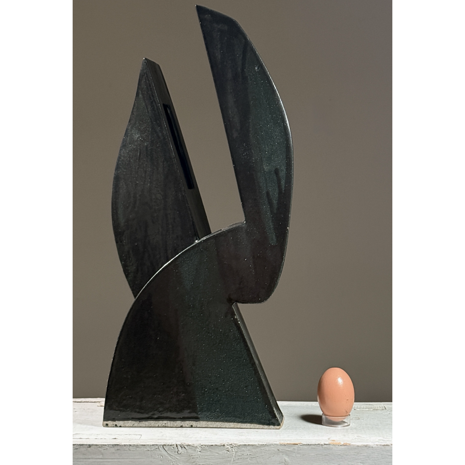 Postmodernist sculptural ceramic ikebana vessel. Glossy black and subtle green glaze with egg for size reference.