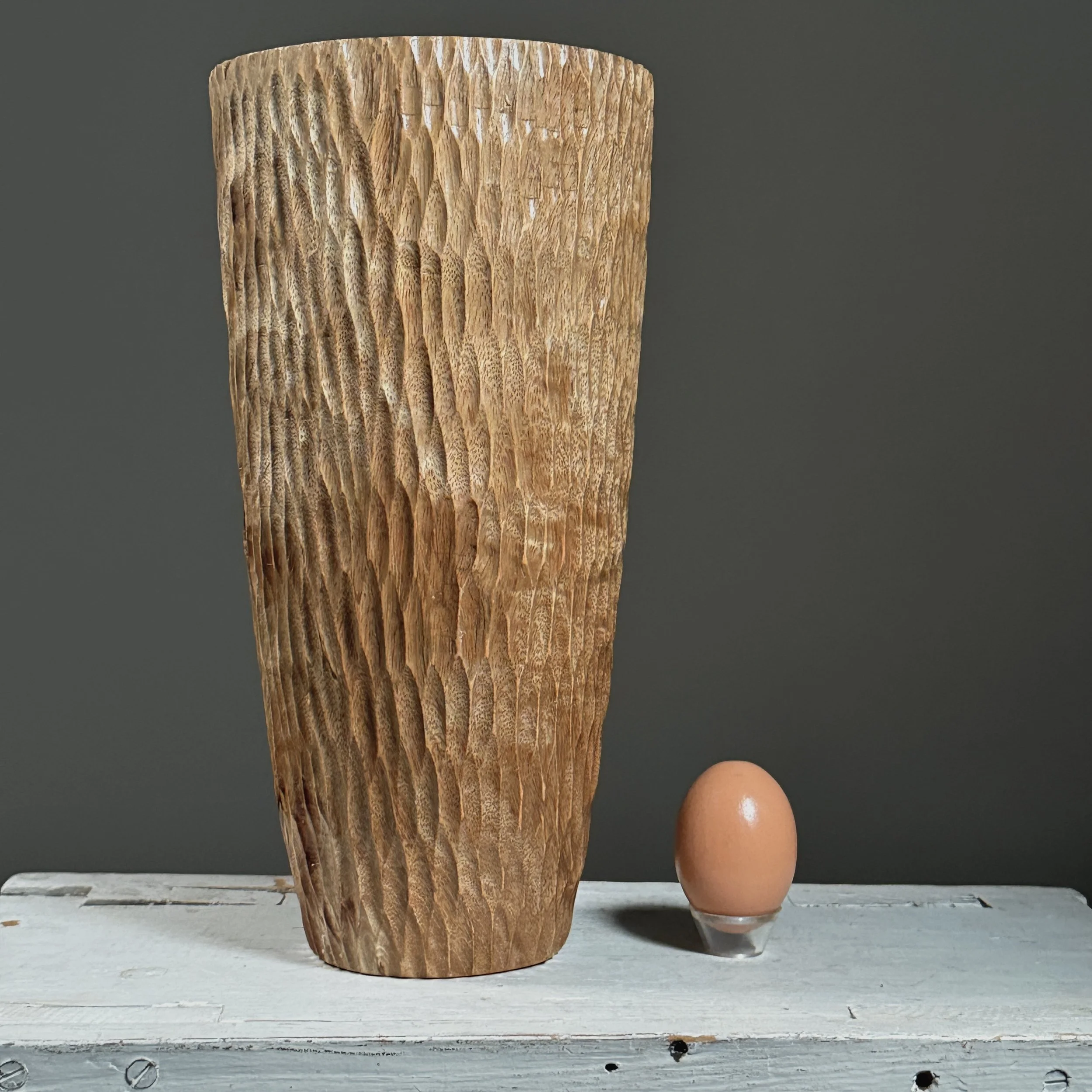Front view of a vintage folk art chip-carved cylindrical wood vase with egg for size reference.