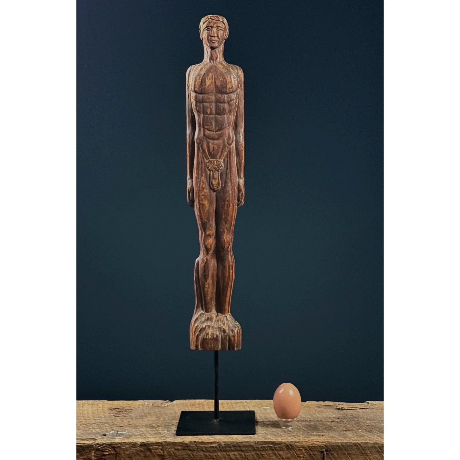 Front view of a vintage hand-carved wooden folk art nude male figure with egg for size reference.