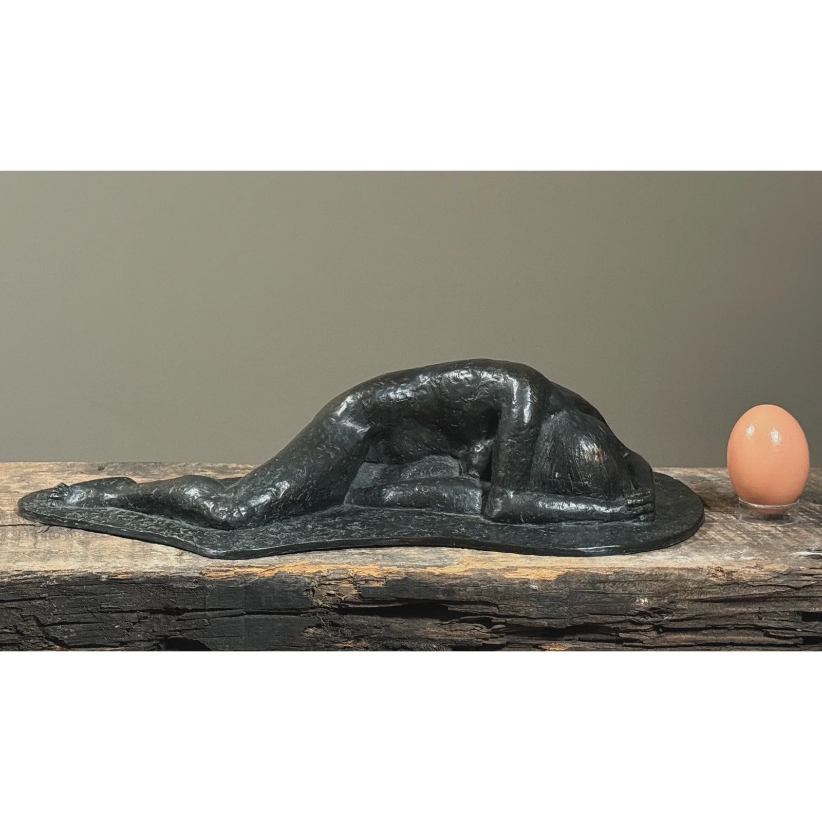 Side view of bronze woman lying with head in arms, Rodin-inspired style with egg for size reference.