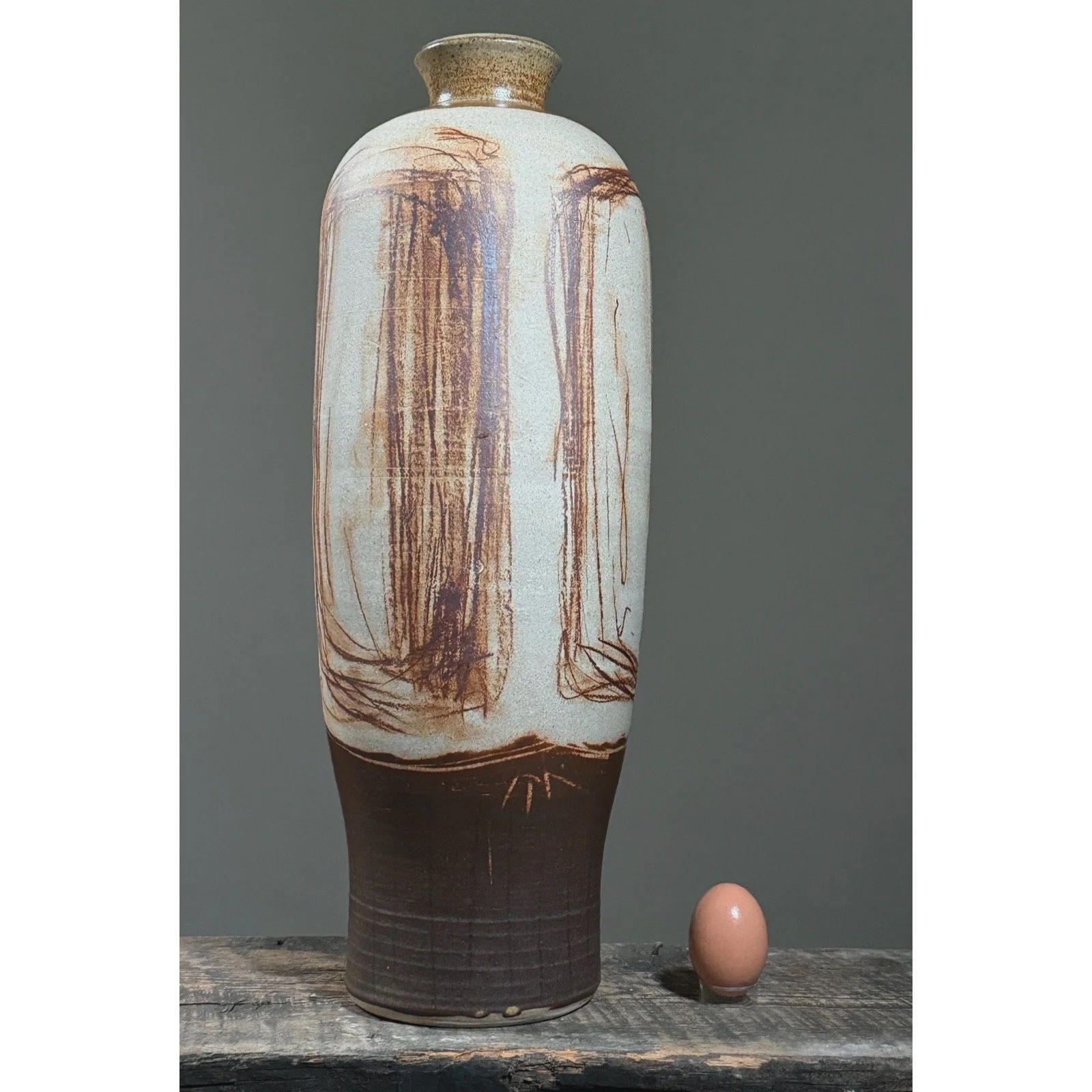 Studio pottery vessel with sketch-like abstract detailing with egg for size reference.