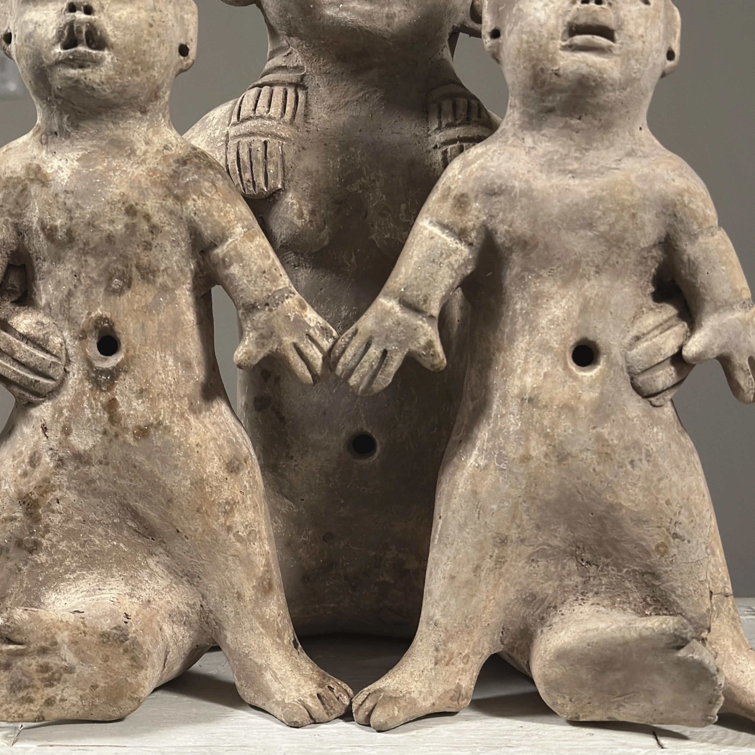 Detail of Antique Olmec style folk art baby sculpture, three terracotta figures, wood fired