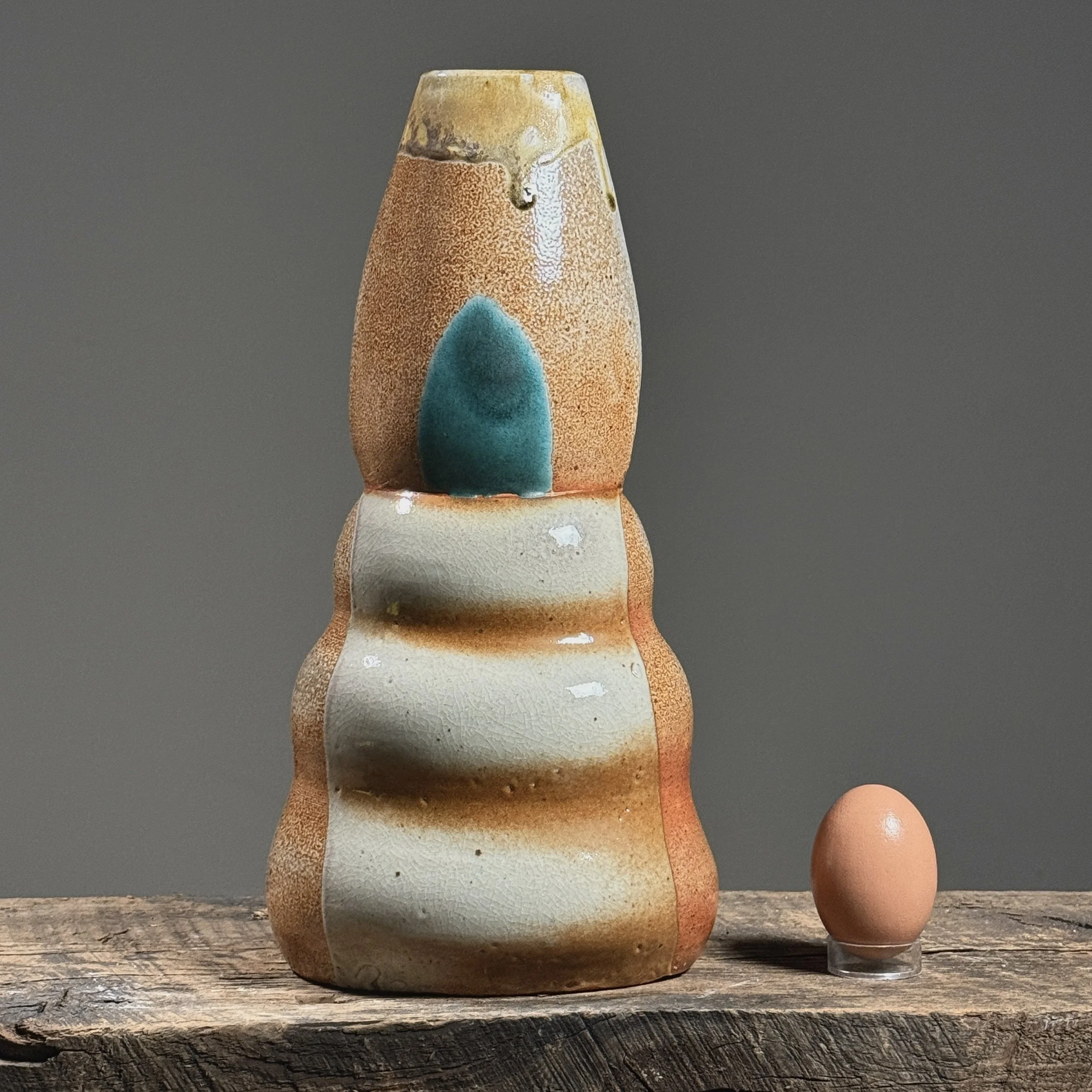 Front view of a vintage postmodernist biomorphic vase with graduating bulges with egg for size reference.