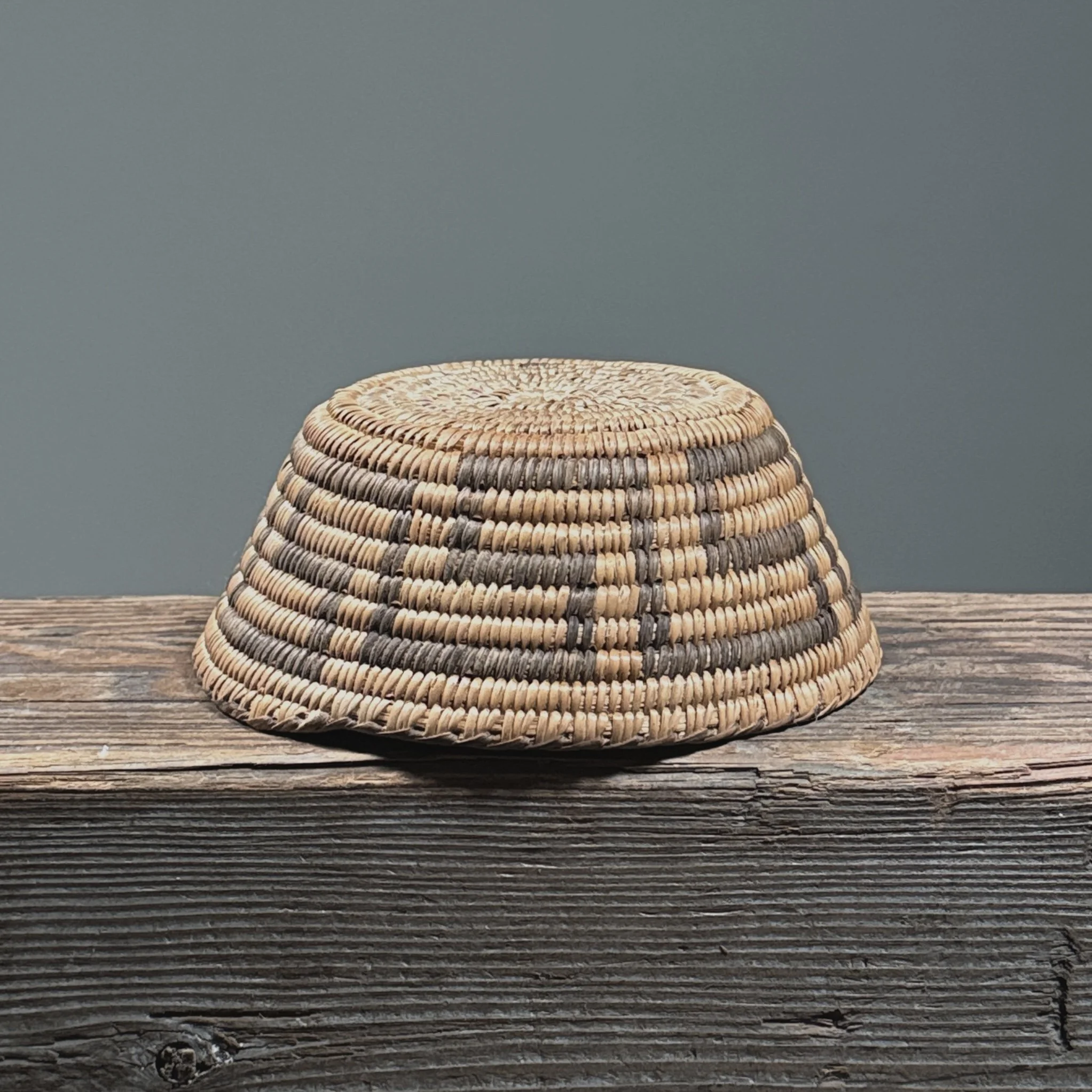 Side view of basket. Shallow form. Flared sides. Dark and light fiber pattern.