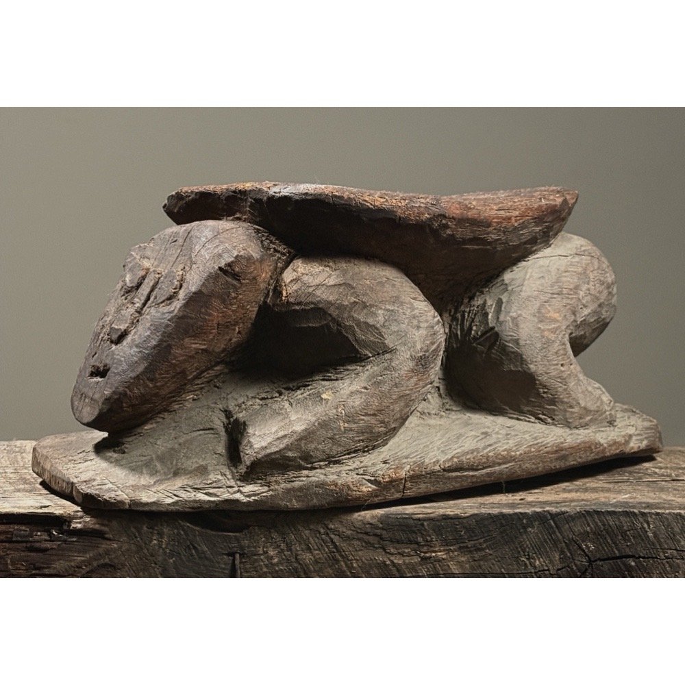 Three-quarter view of a hand-carved wooden stool with figural support and carved top surface