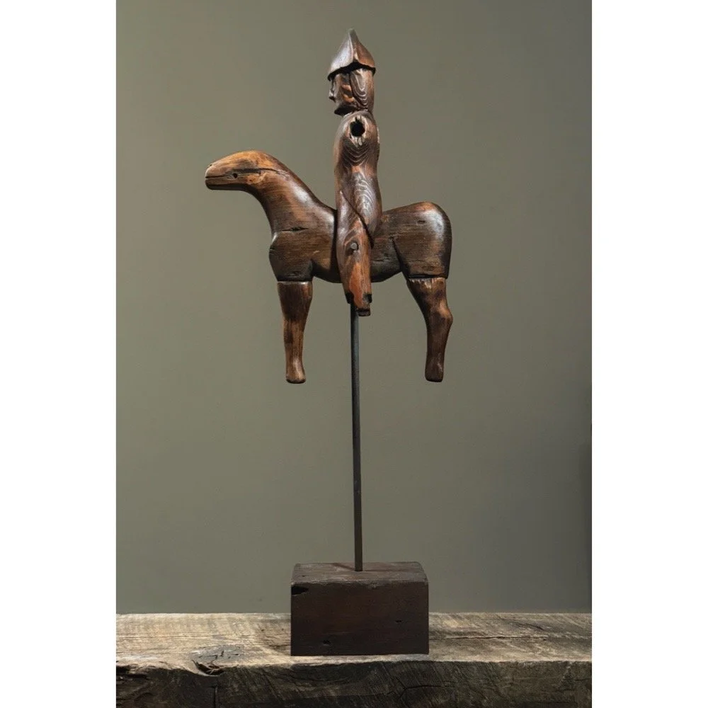 Side view of carved wooden soldier riding horse on plinth.