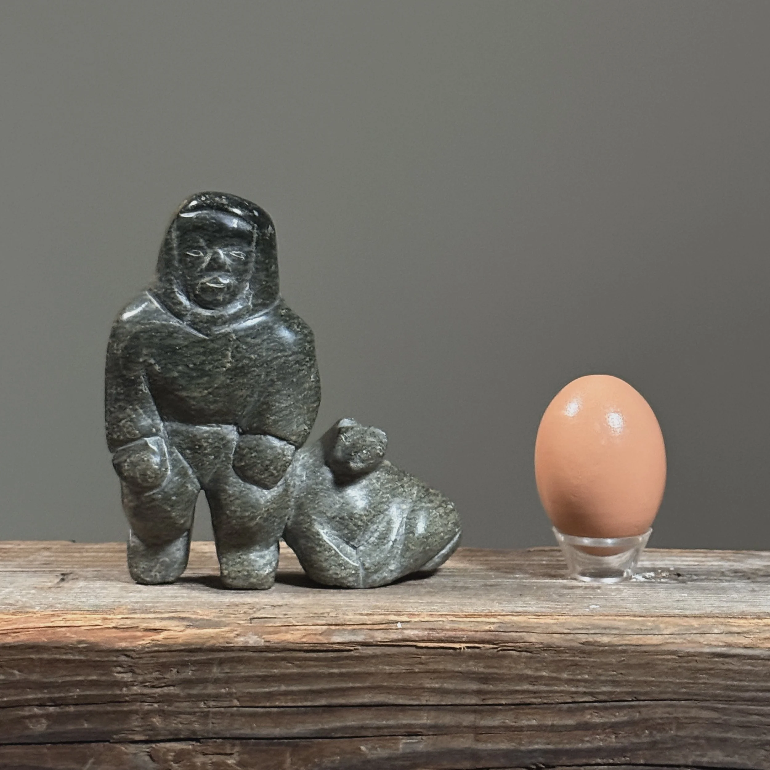 Full frontal view of a vintage Inuit hand-carved green soapstone sculpture of a human figure with a seal