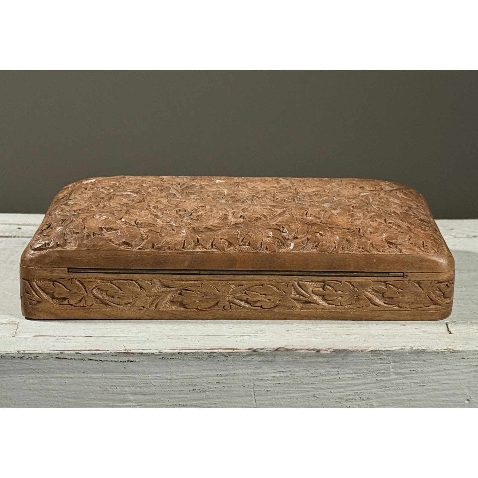 Full frontal view of a vintage hand-carved folk art lidded box with intricate foliage detail on the lid