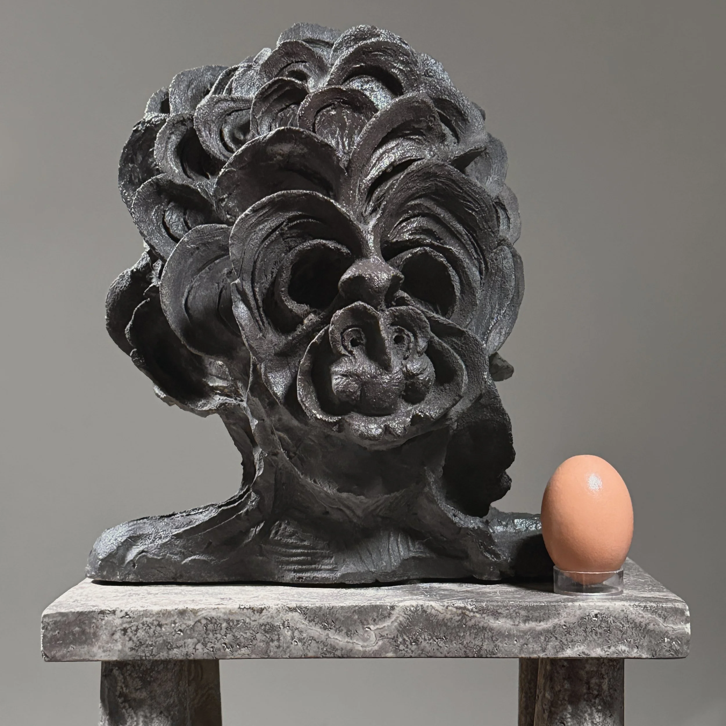 Front view of black clay portrait sculpture. Undulating wave surface. Abstract Expressionist.  Pictured with egg for size reference.