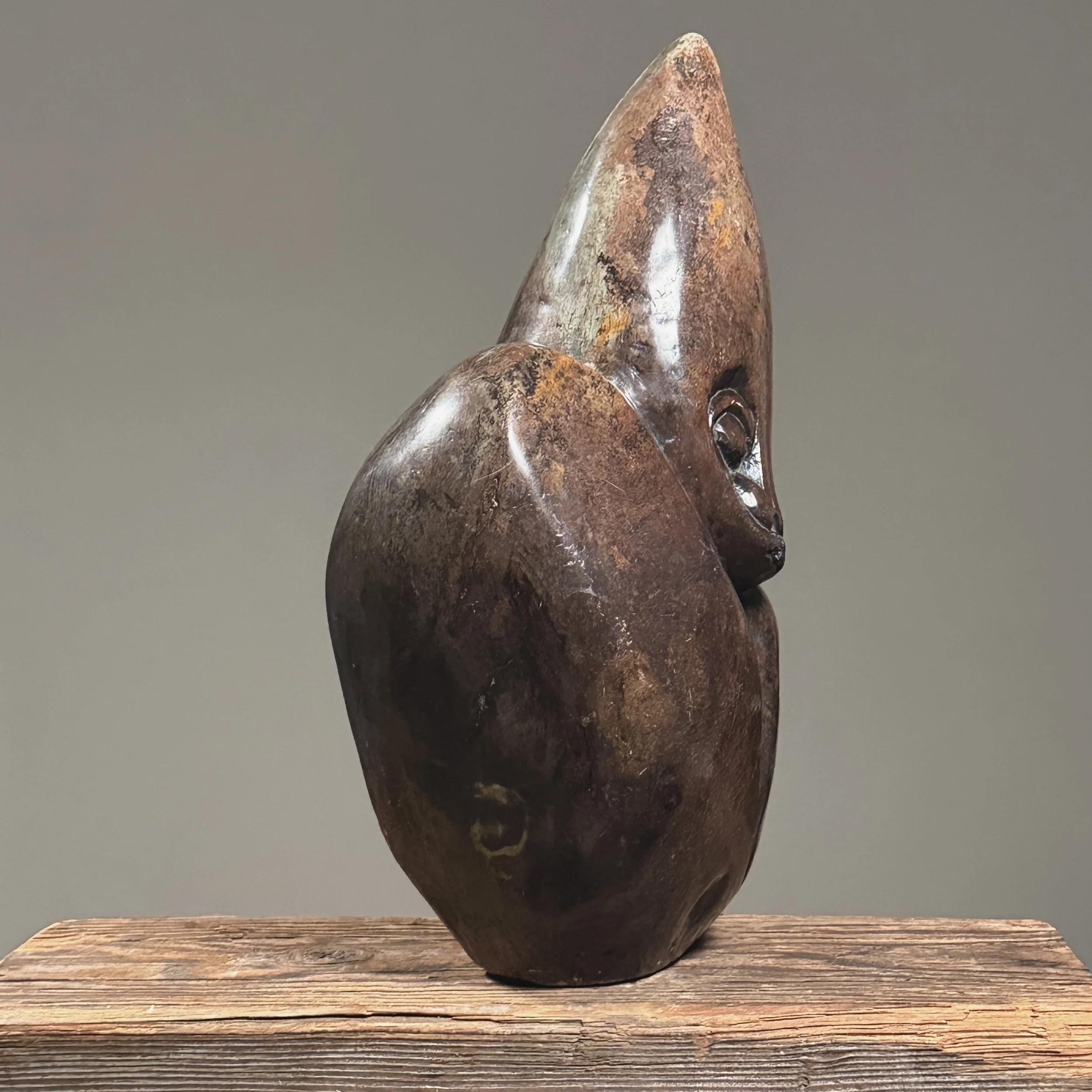 Side view of vintage figurative Shona stone sculpture, 13.5 inches tall, elongated head, puce-colored material.