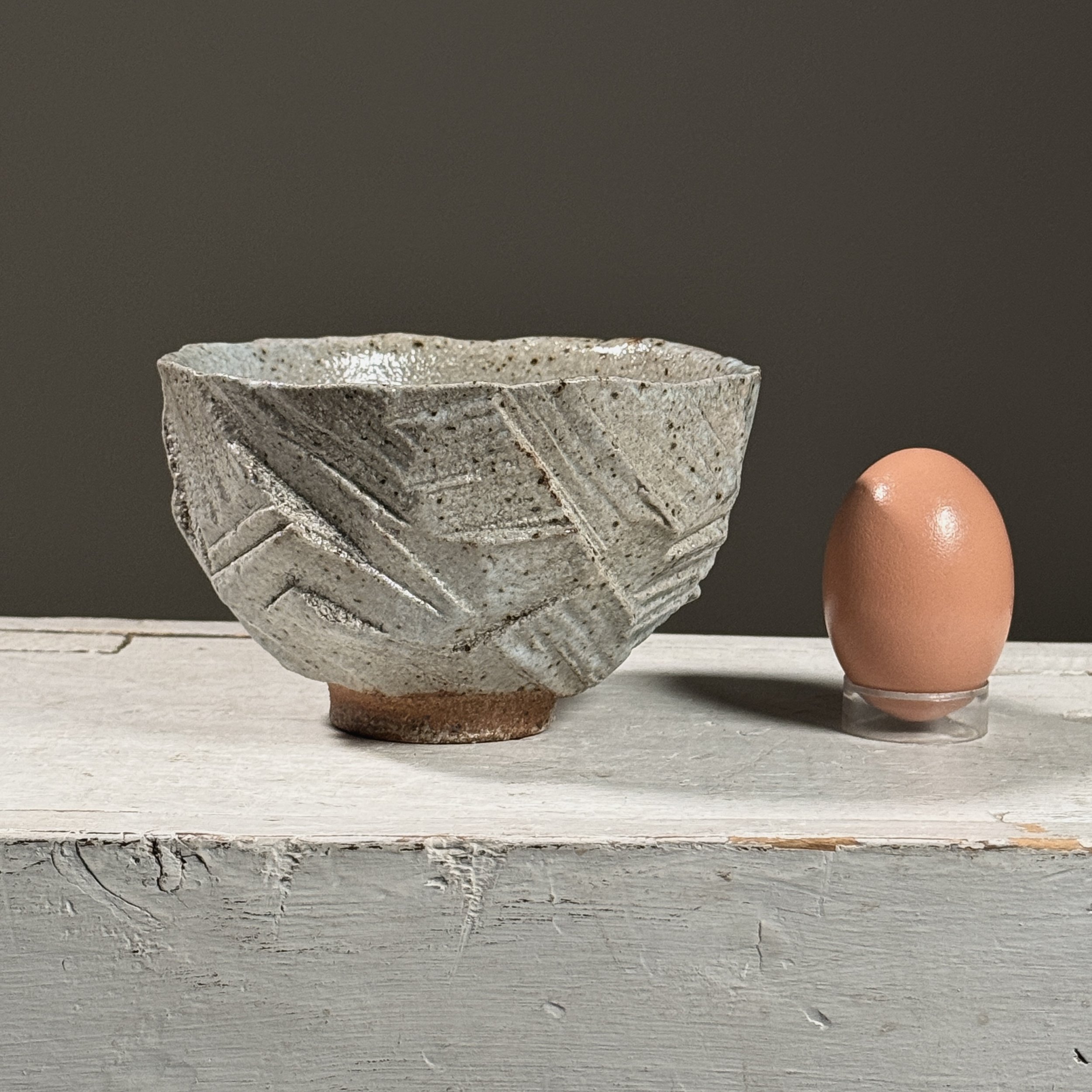 Front view of a vintage Brutalist geometric carved ceramic footed bowl with egg for size reference.