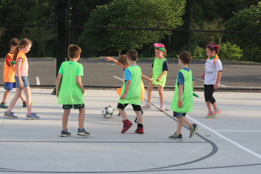Young kids having a soccer scrimmage on a concrete court.