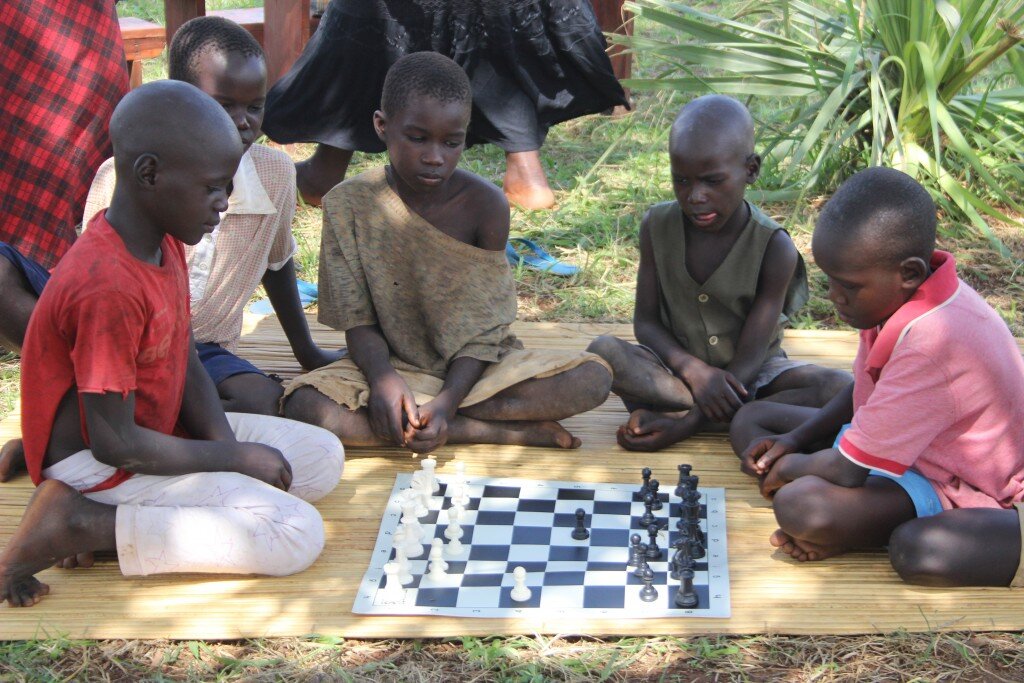 A group of young boys in Gulu sitting on a straw mat playing chess. 