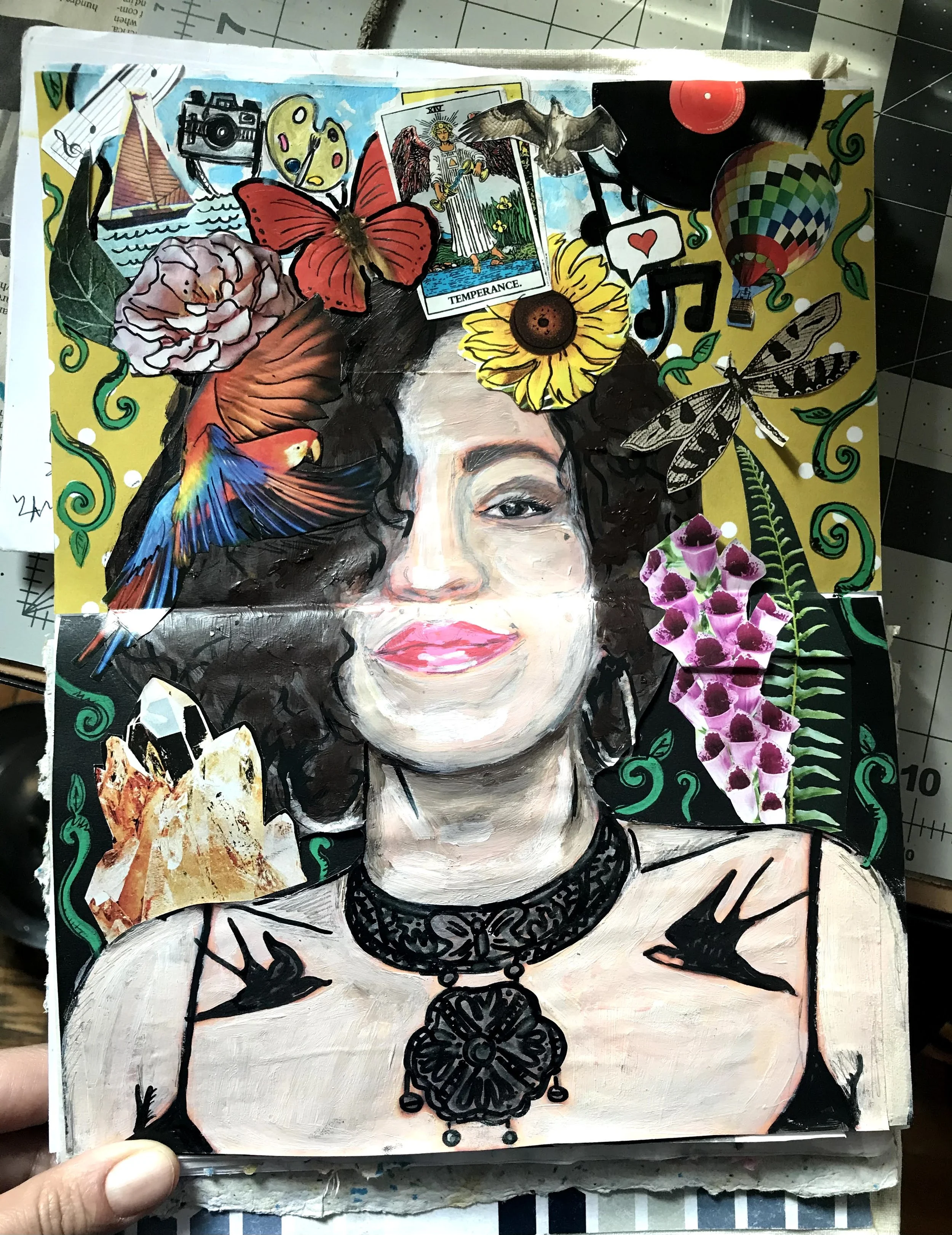 Mixed media portrait of artist with curly hair, wearing a black lace choker and top, surrounded by colorful collage elements like flowers, animals, and symbols.