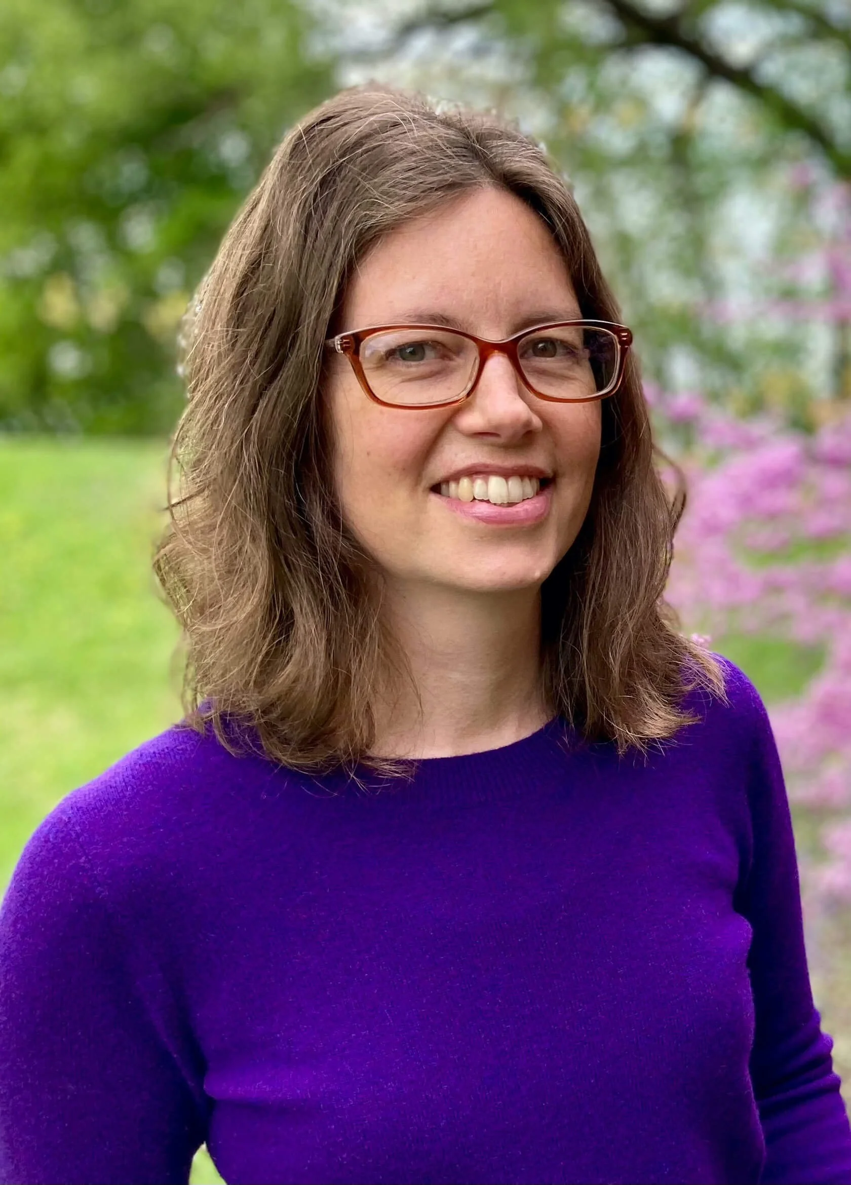 Bronwyn Shiffer, Boston, MA depression therapist, white woman with brown hair wearing glasses and a purple sweater, standing near a pink flowering tree. Therapy for depression in Boston MA can help decrease isolation. | 02481 | 02493 | 01890