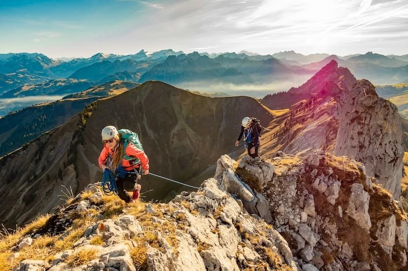 Two people in hiking gear walking the narrow ridge of a mountain representing the courage it takes to address work burnout. Depression therapy in Boston, MA can help decrease burnout on the job. | 02481 | 02493 | 01890