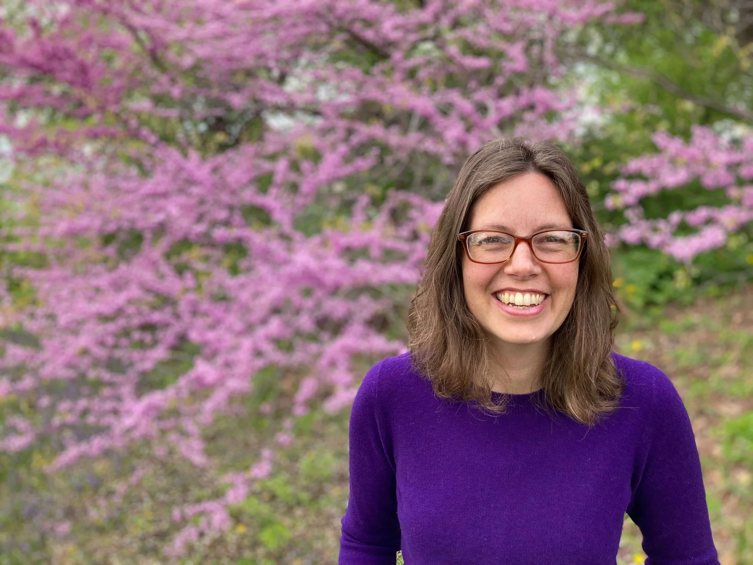 Bronwyn Shiffer, MA depression therapist, white woman with glasses and brown hair wearing a purple sweater next to flowering tree.  | 02481 | 02493 | 01890