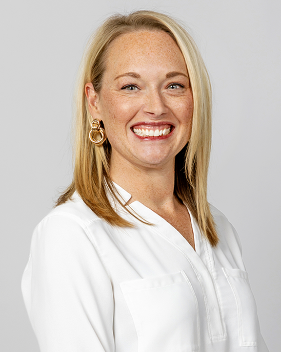 A woman with blonde hair smiling, holding a speech bubble sign with a stylized figure inside.