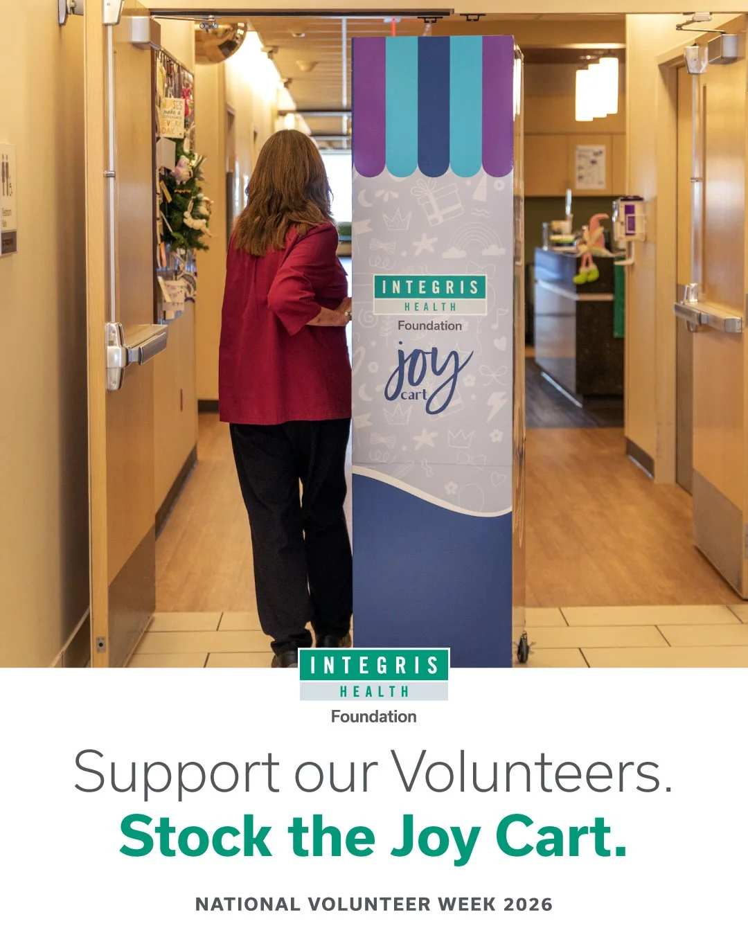 A woman in a red blazer standing next to a colorful donation cart labeled 'Joy Cart' in a hospital or community center hallway, supporting volunteers during National Volunteer Week 2026.