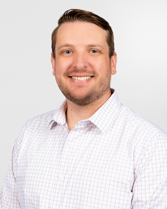 A smiling man wearing a purple T-shirt and a badge, holding two teal speech bubble signs with icons and text. One sign says 'PROJECT: YOU & I' and the other has a head with gears inside, representing ideas or thinking.