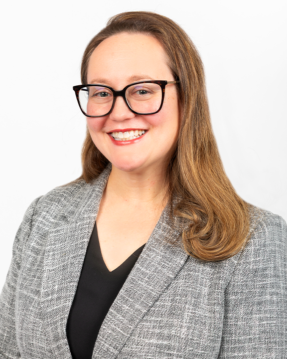 A woman with long light brown hair, wearing glasses and a black blazer, holding a sign with a white stethoscope illustration on a teal background.