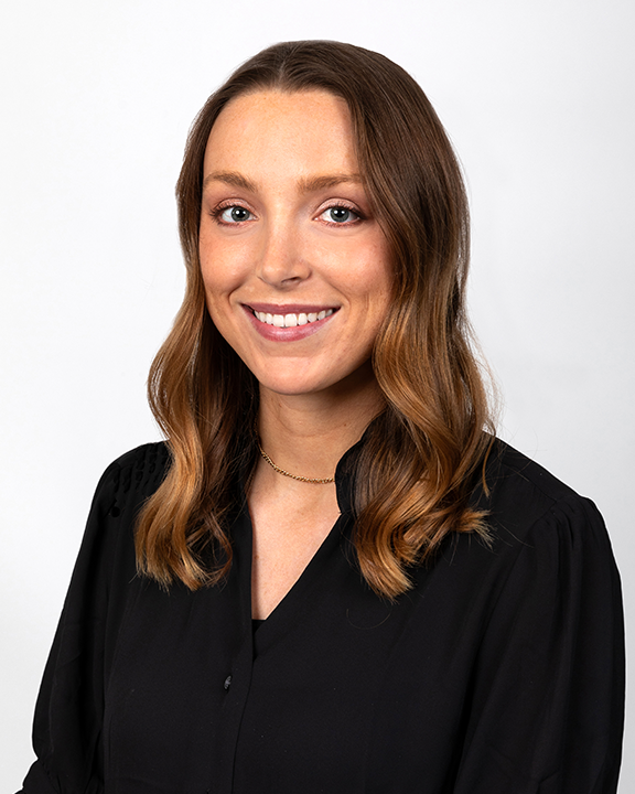 A woman with brown hair smiling, holding signs with a candle and a heart with a heartbeat line, representing health or awareness themes.