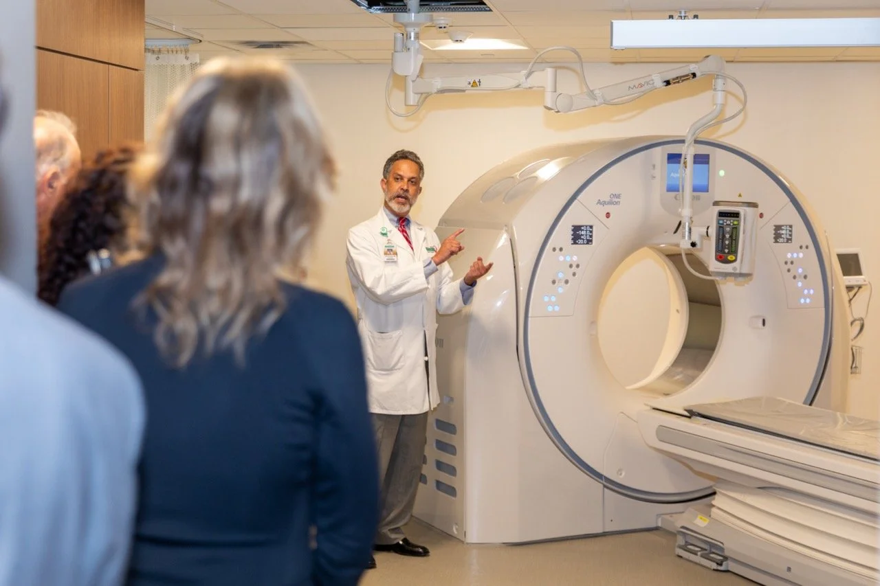 A healthcare professional explains a medical imaging machine to a group of people in a hospital or clinic.