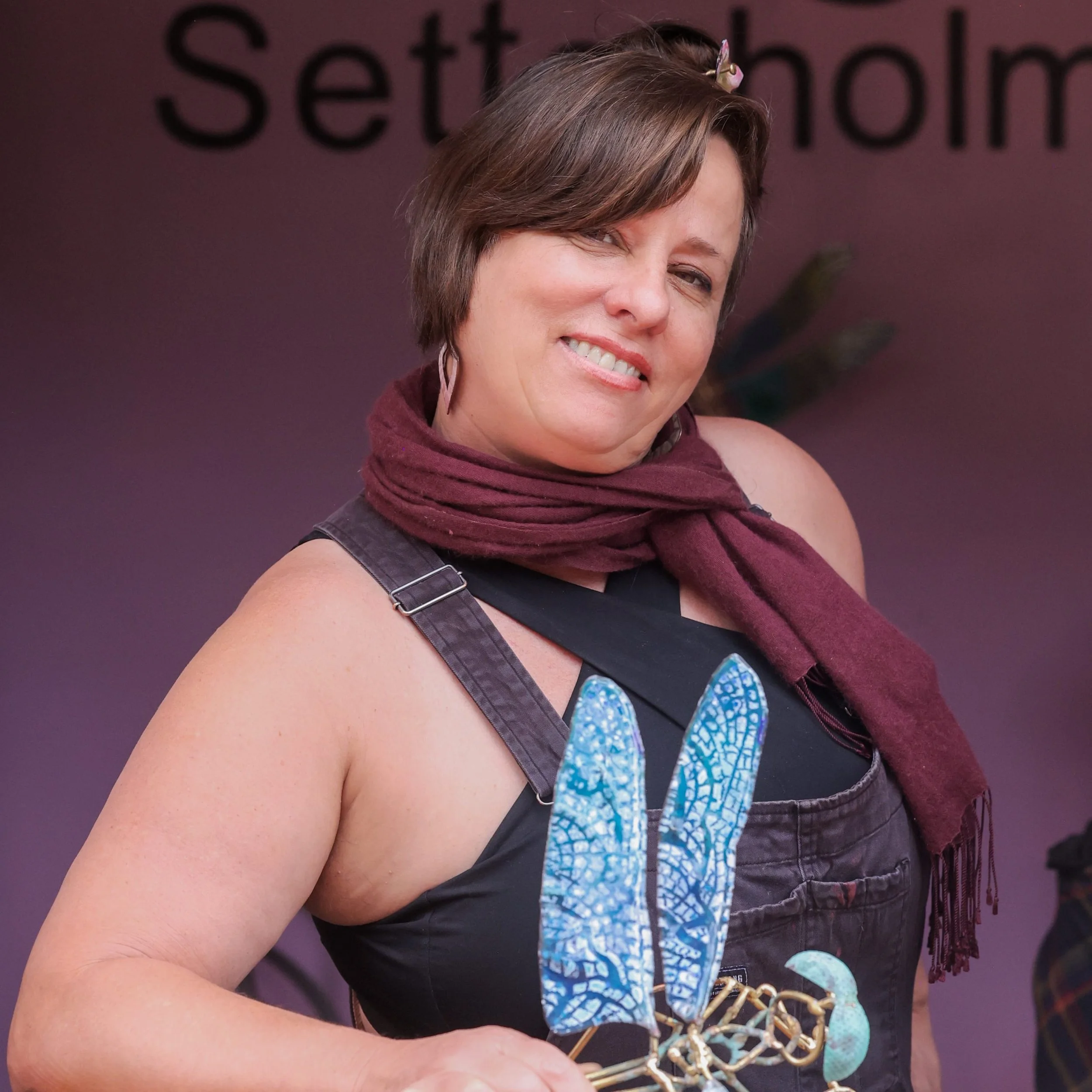 Artist Julie Setterholm at the Sawdust Art Festival holding one of her blue enamel-on-copper Lovebug pieces